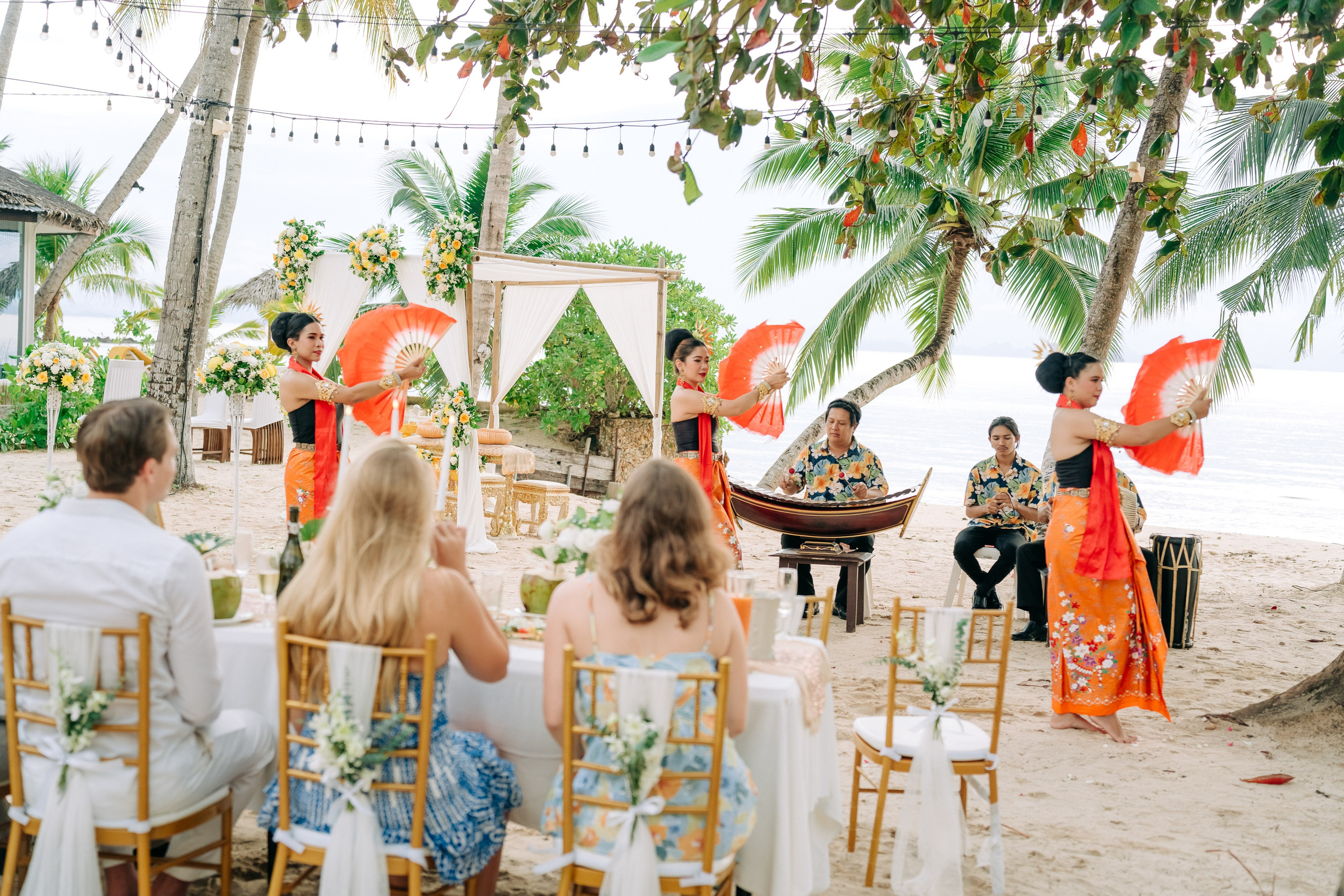 Couple taking part in a traditional Buddhist wedding ceremony on a tropical beach in Koh Samui, Thailand, with monks, flowers, and ocean views.