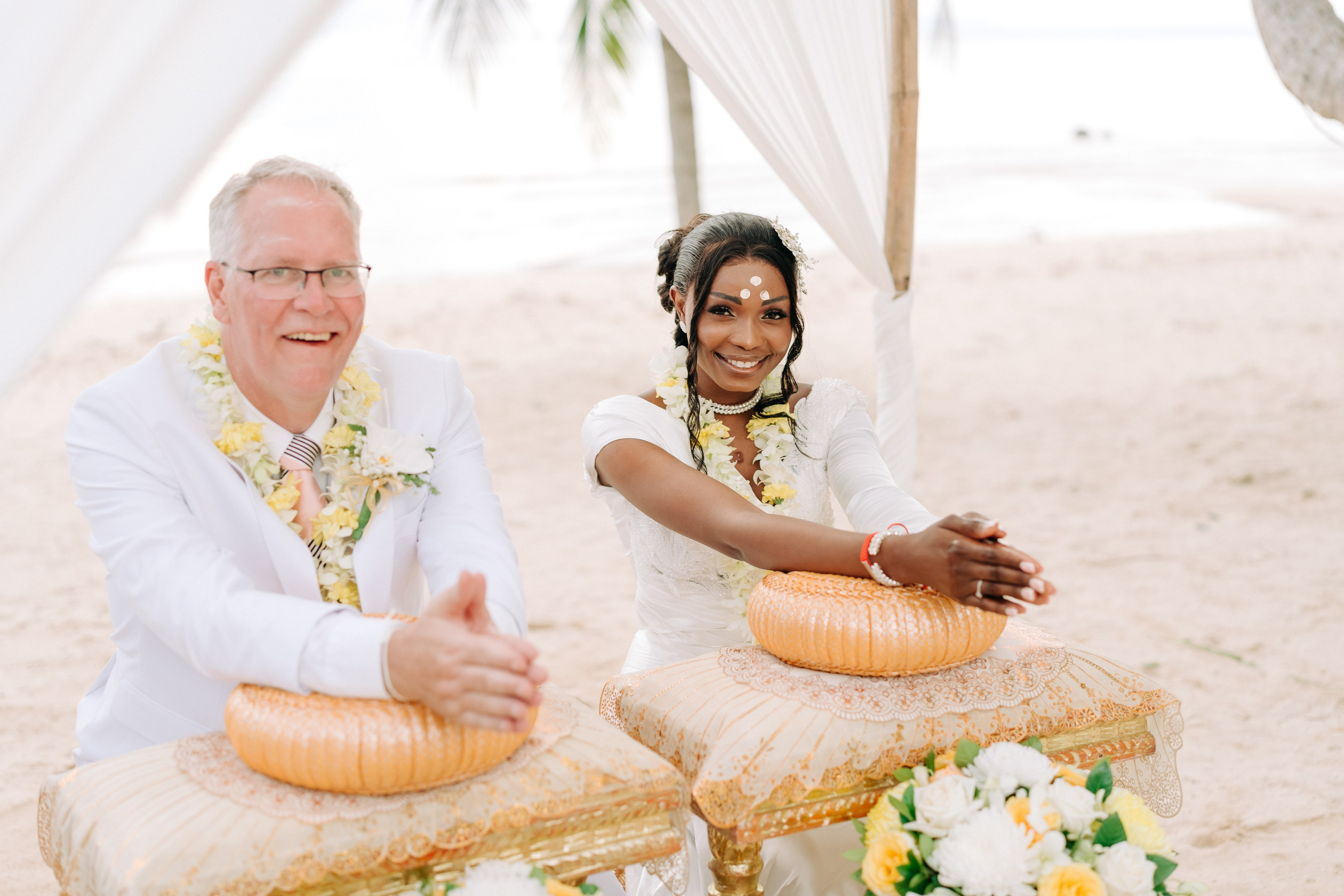 Couple taking part in a traditional Buddhist wedding ceremony on a tropical beach in Koh Samui, Thailand, with monks, flowers, and ocean views.