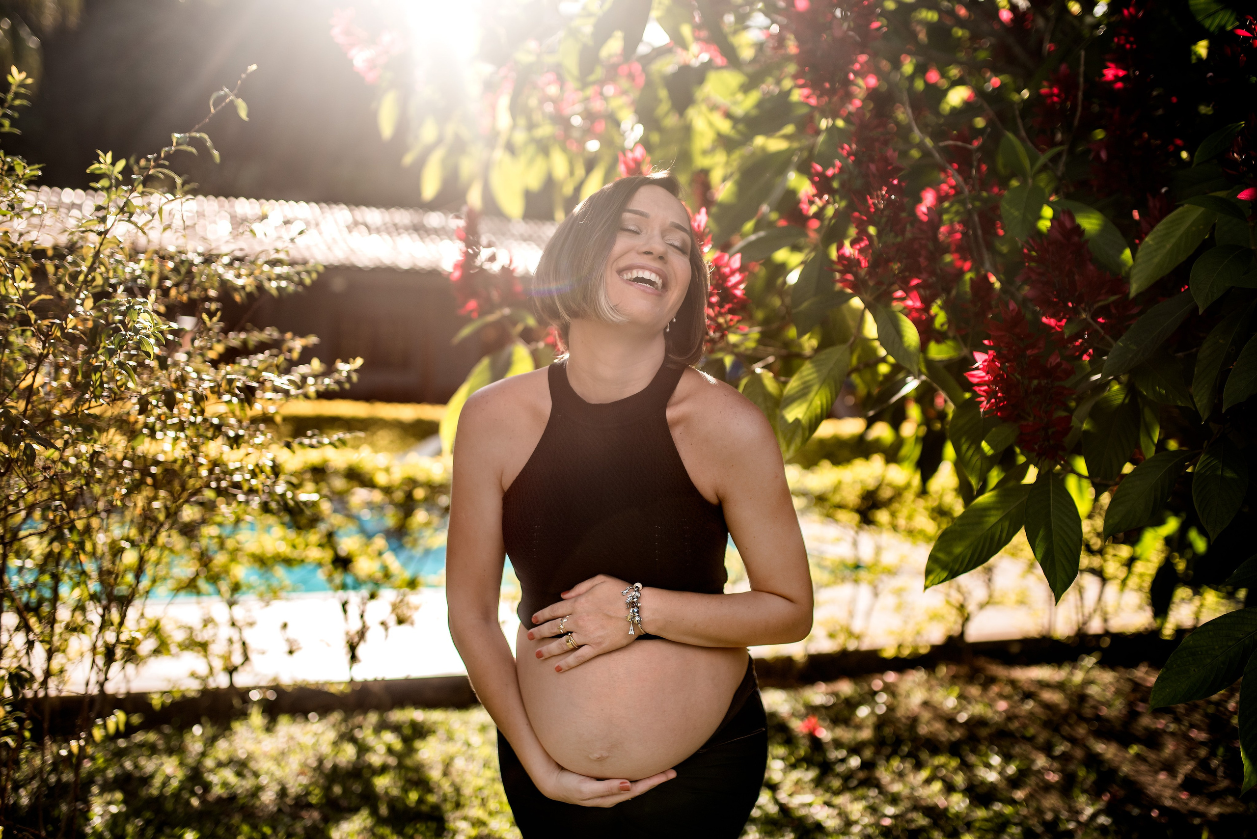 Ensaio gestante externo em Juiz de Fora, mãe sorrindo com flores vermelhas ao fundo