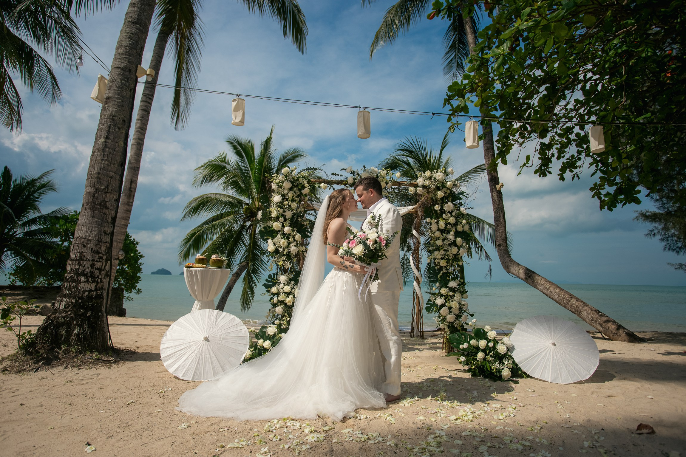 Bride and groom celebrating a beach wedding with their children in Koh Samui, Thailand, surrounded by tropical scenery and ocean views