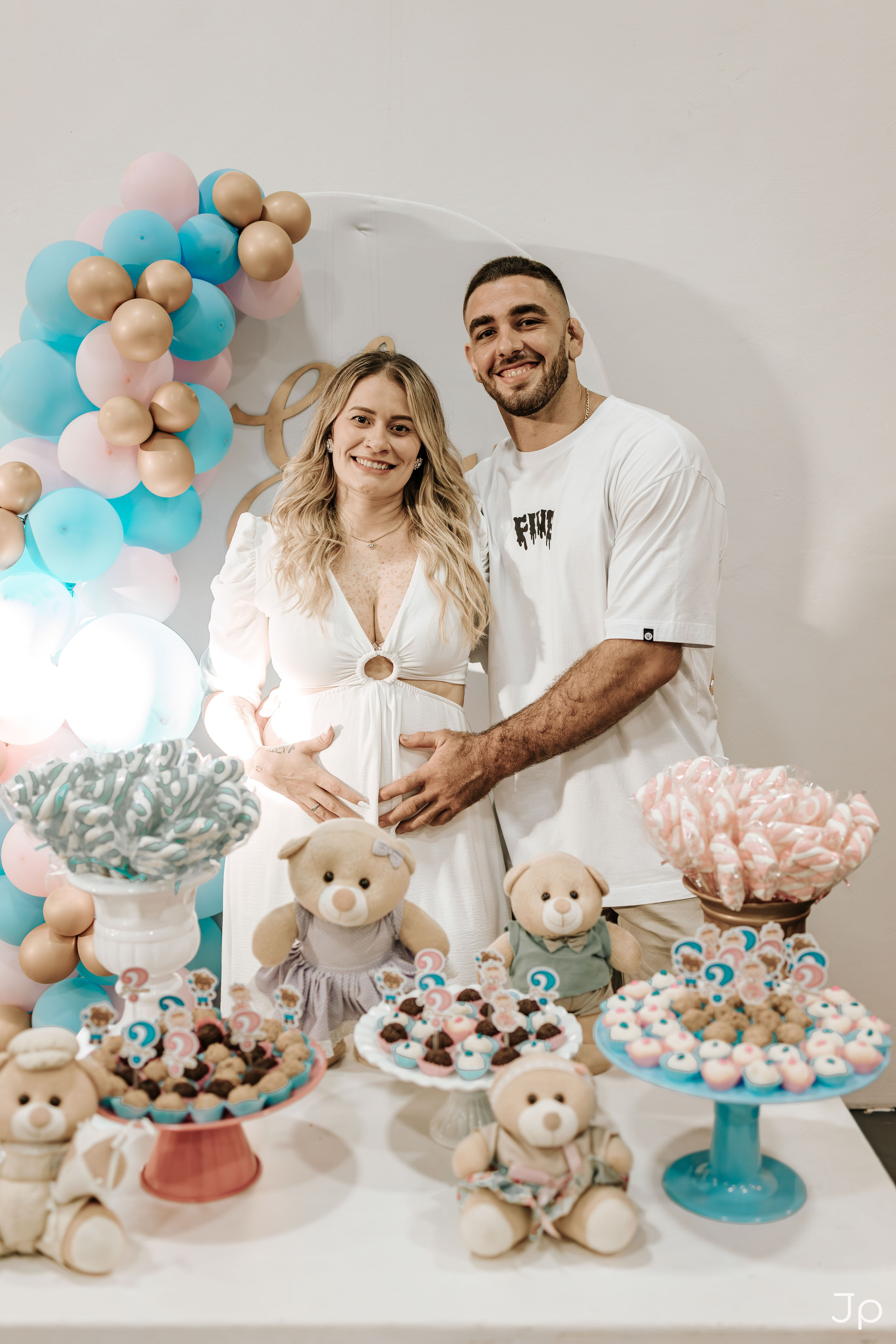 Gestante sorrindo ao lado do seu marido na decoração azul e pelúcia de urso.
