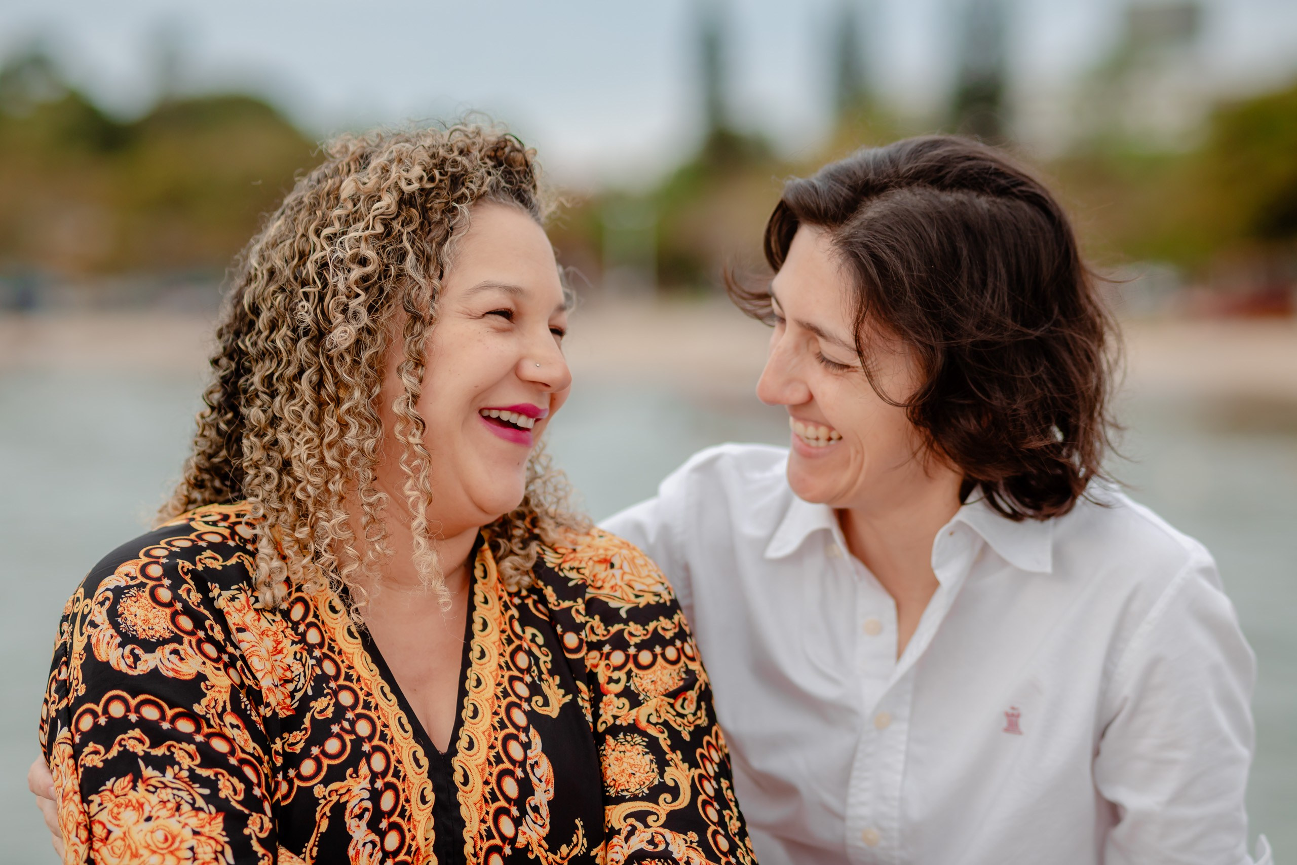 Fotógrafo ensaio gestante em Penha; retrato próximo e espontâneo do casal sorrindo com cumplicidade ao ar livre, destacando a conexão e a alegria.