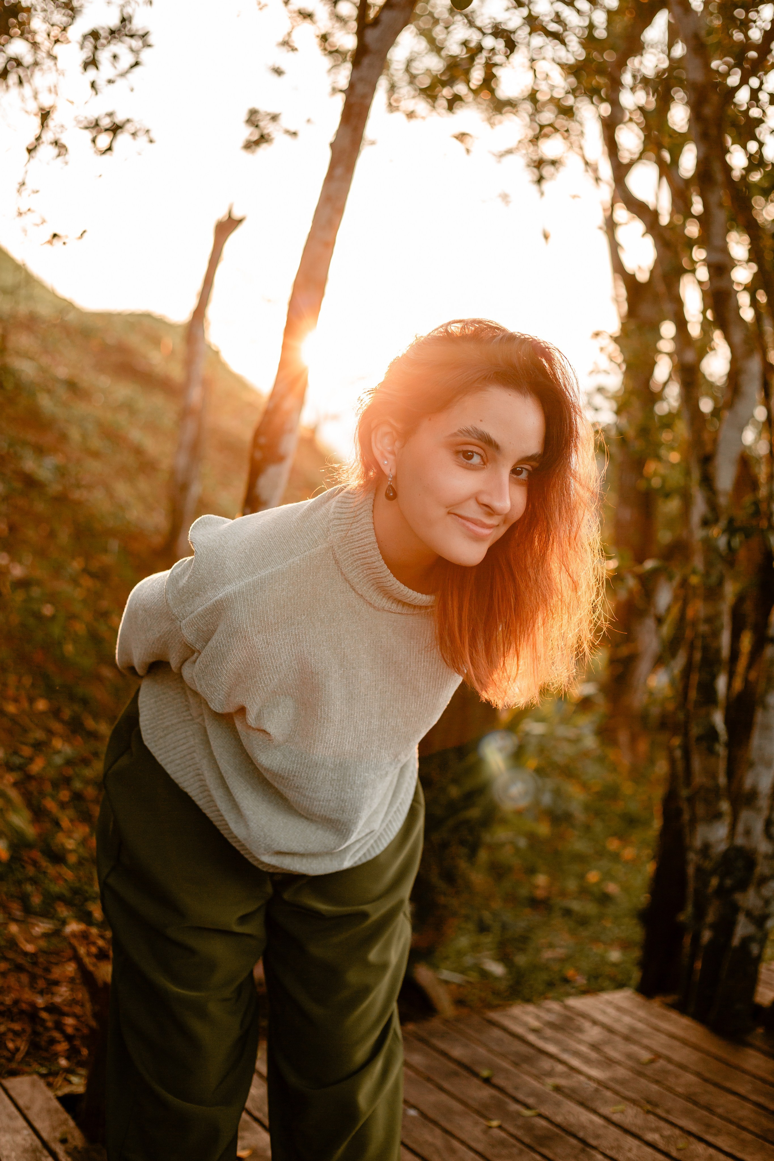Mulher olhando pra câmera com pôr do sol ao fundo.