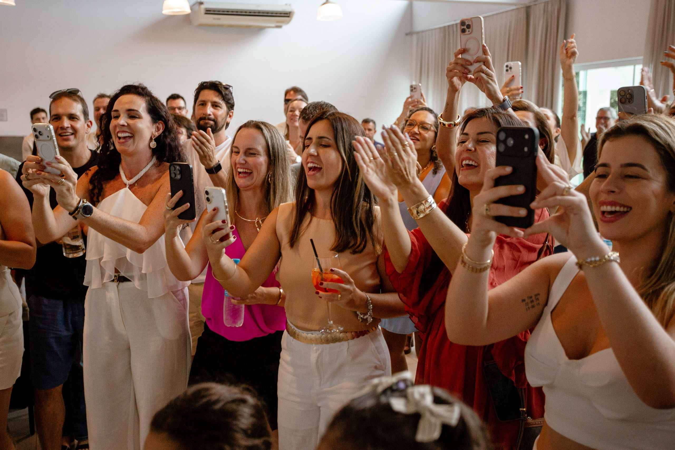 Fotografia de cobertura de festa de aniversário em Itajaí capturando a alegria e a animação dos convidados cantando parabéns e registrando o momento com os celulares.