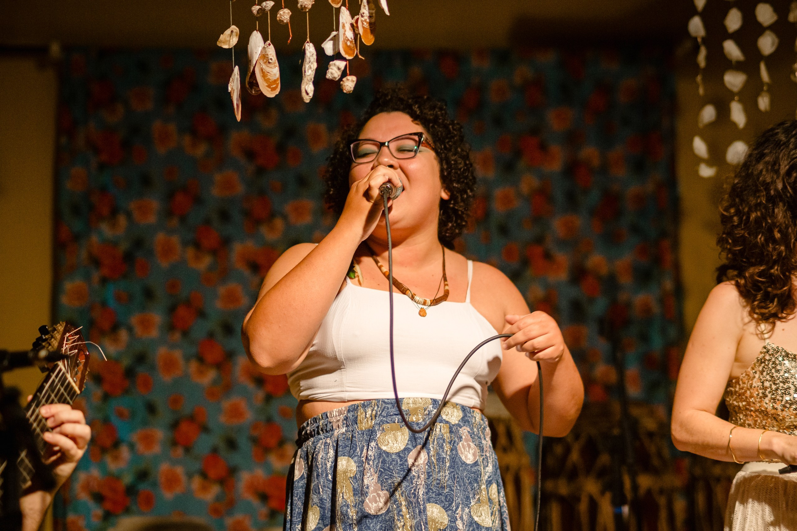 Fotógrafo de show em Balneário Camboriú; cantora convidada cantando com expressão emotiva no microfone durante a apresentação no bairro da Barra para o projeto de Joana Gaia.