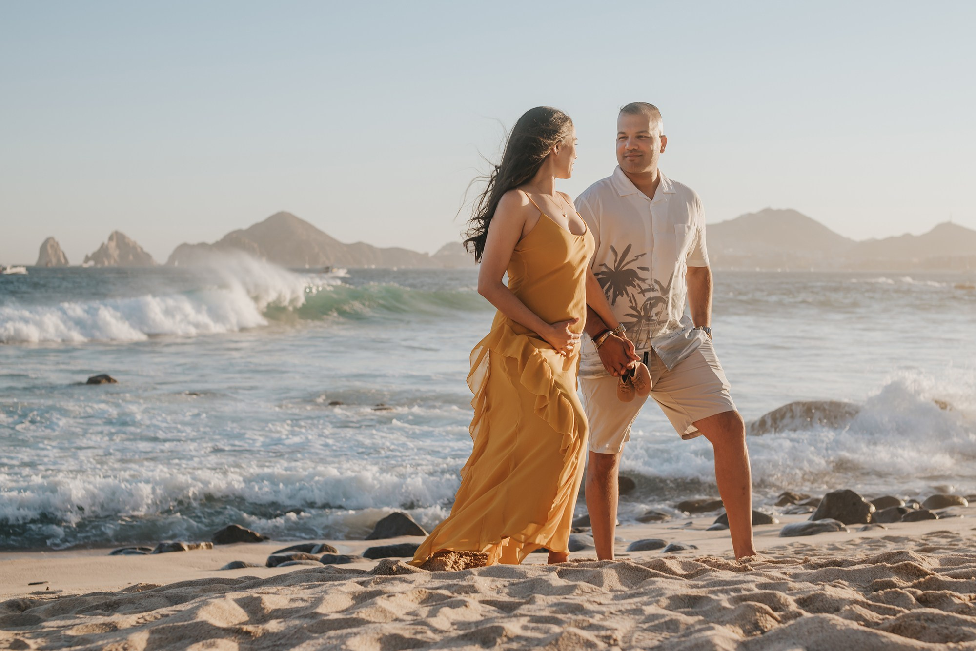 Expecting parents holding baby shoes during maternity photoshoot in Los Cabos Mexico