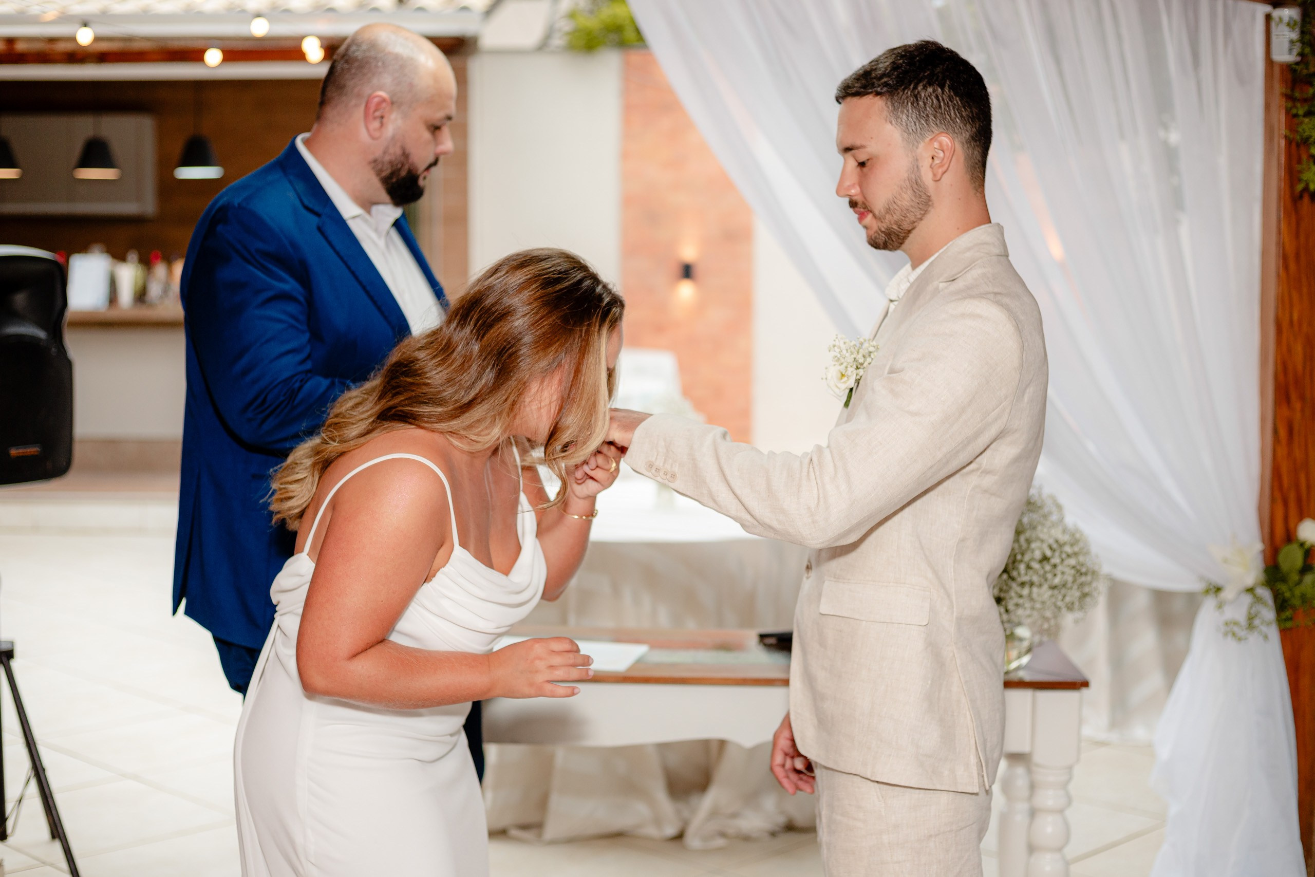 Fotógrafo de casamento em Bombinhas; o noivo beija com carinho a mão da noiva junto ao altar, com a presença do celebrante ao fundo.