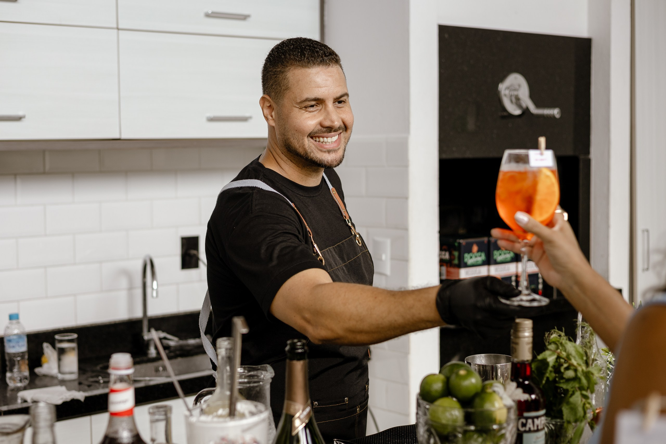 Fotografia de cobertura de festa e evento em Itajaí mostrando o bartender sorridente entregando um coquetel com laranja a uma convidada no bar.