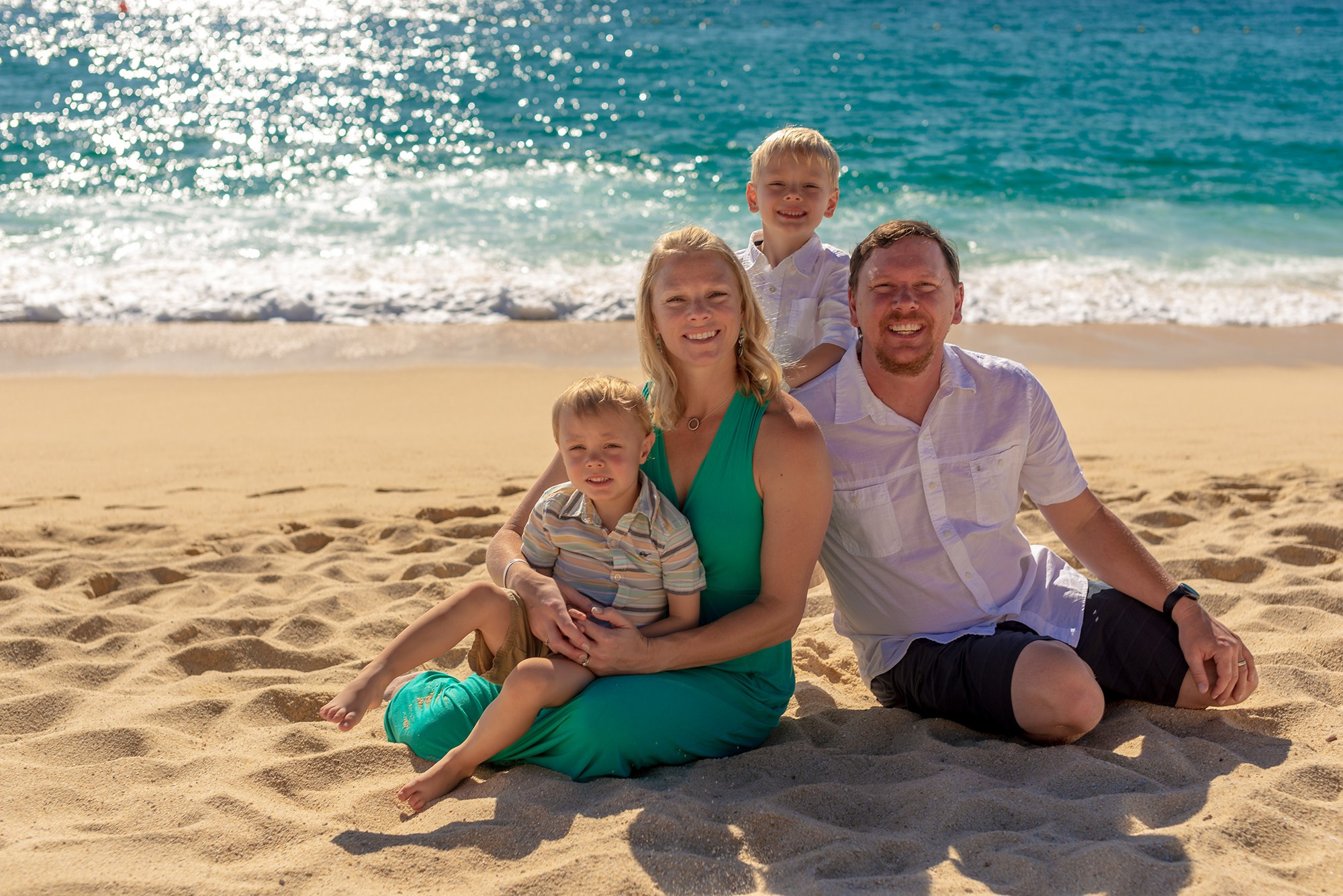 Family beach portrait in Los Cabos – family of four with young children sitting on the sand, joyful and natural destination family photography