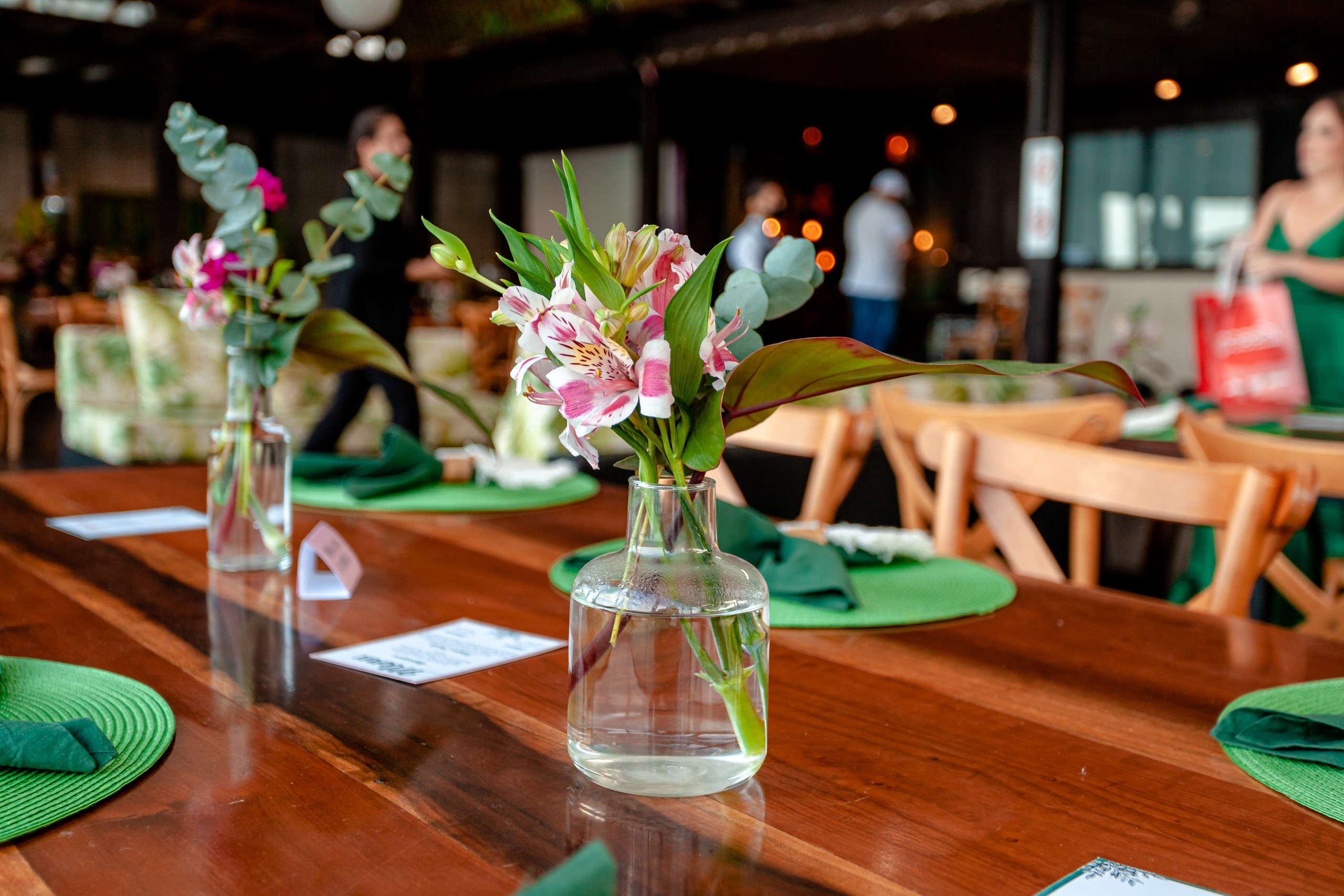 Fotógrafo festa de formatura em Balneário Camboriú; arranjos florais delicados em garrafas de vidro decorando as mesas de madeira no Bali Bistro Beach.