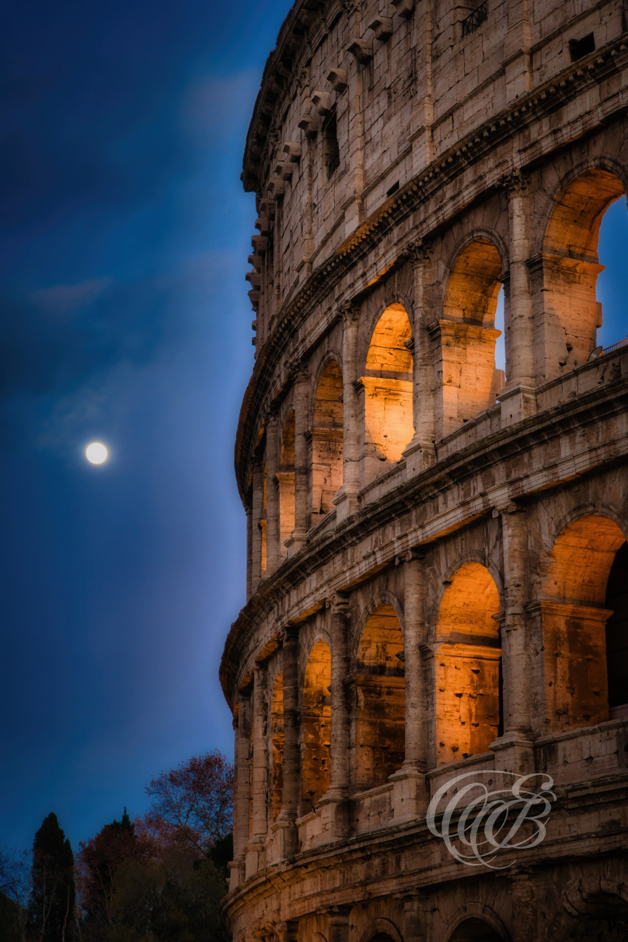 ITALY TRAVEL PHOTOGRAPHY – ITALY – ROME — Colosseum at Dusk with Full Moon — Ancient Roman amphitheater illuminated by dusk light with a full moon rising above, showing arches and exterior stone structure, Rome, Italy — Eduardo Bartoli Photography.