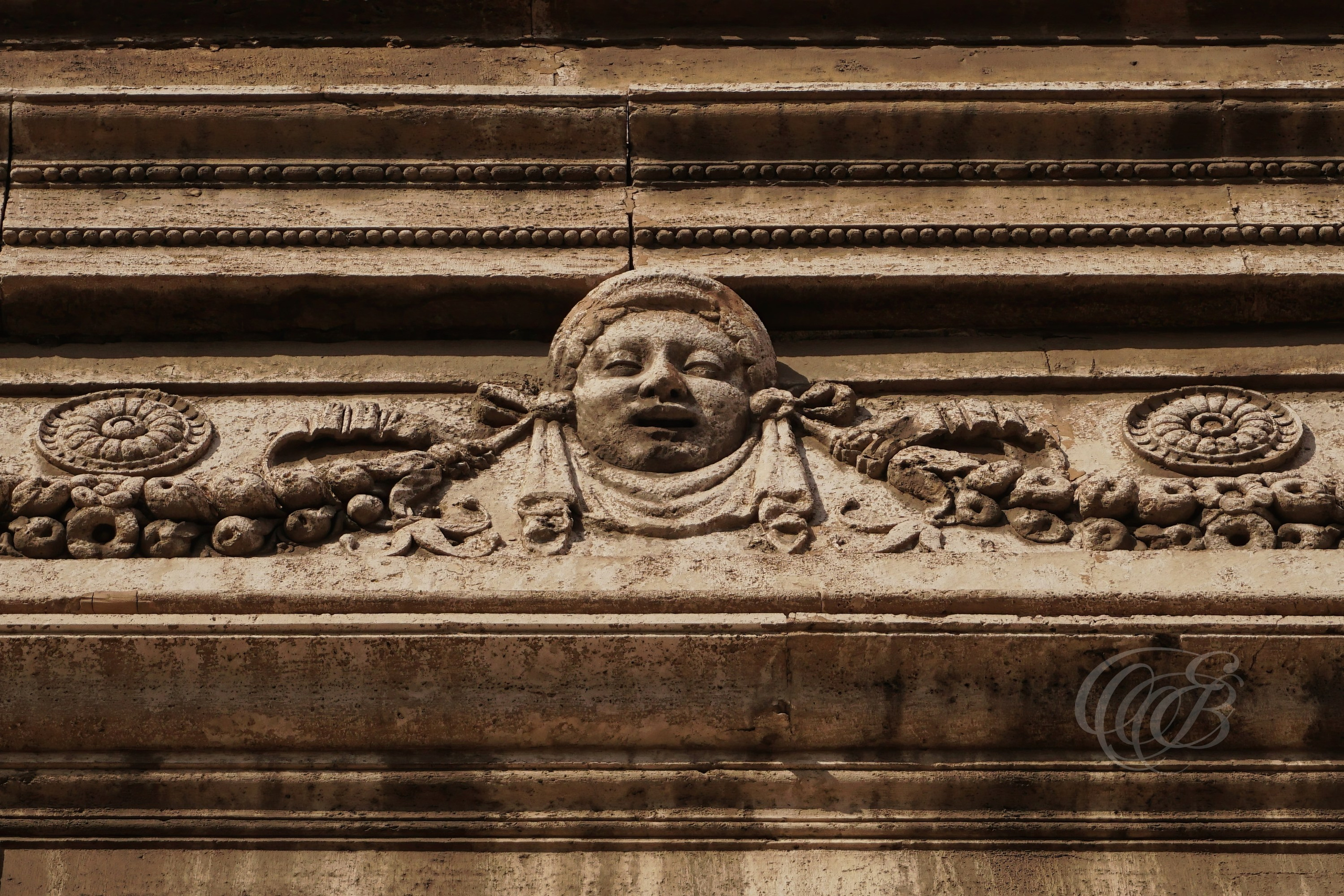 ITALY TRAVEL PHOTOGRAPHY – ITALY – ROME — Bas-Relief Face with Ornamental Details in Trastevere — Sculpted stone face relief on historic building façade in Trastevere, showing ornamental architectural detail and carved decoration, Rome, Italy — Eduardo Bartoli Photography.