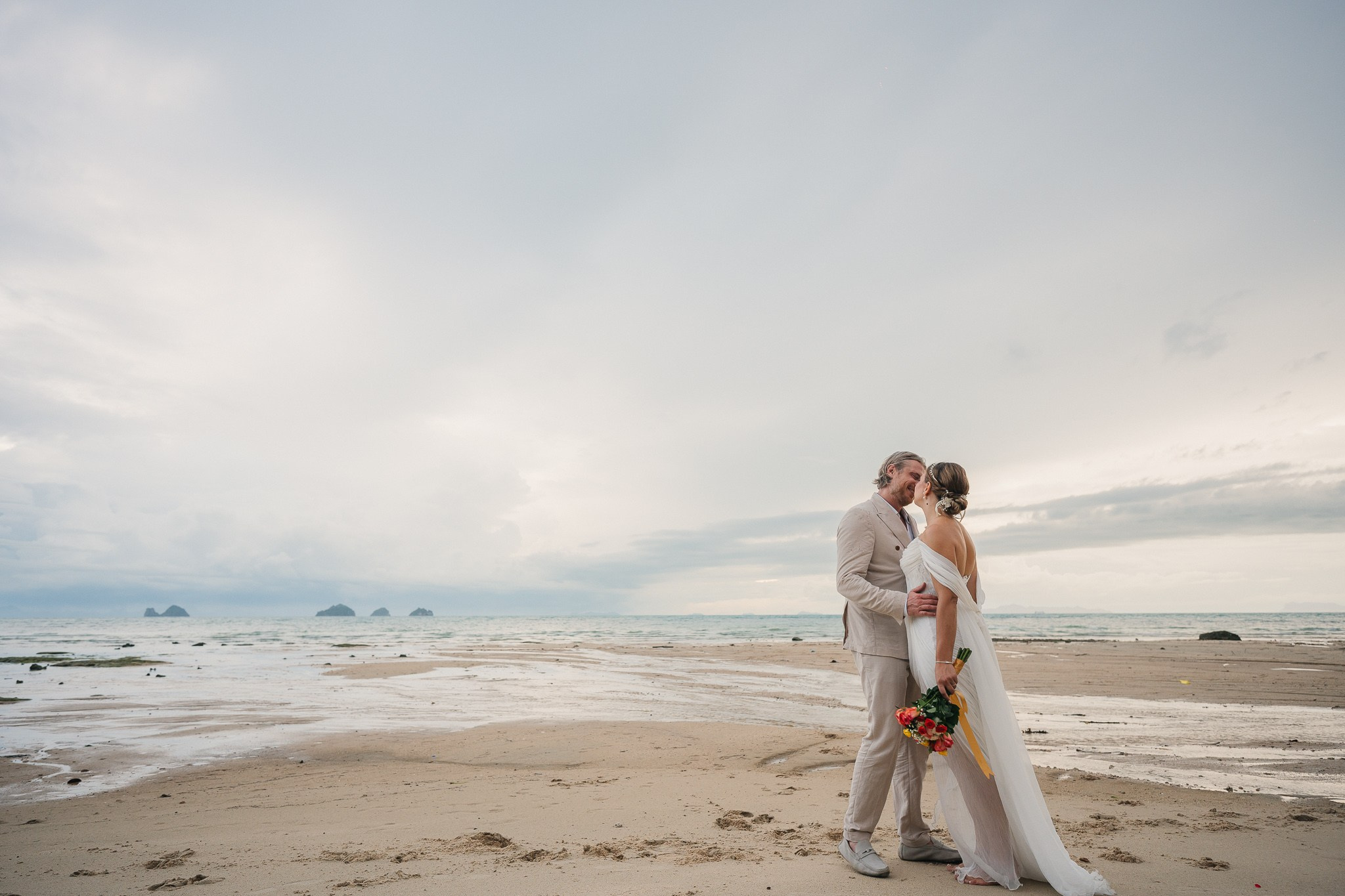 Couple taking part in a traditional Buddhist wedding ceremony on a tropical beach in Koh Samui, Thailand, with monks, flowers, and ocean views.