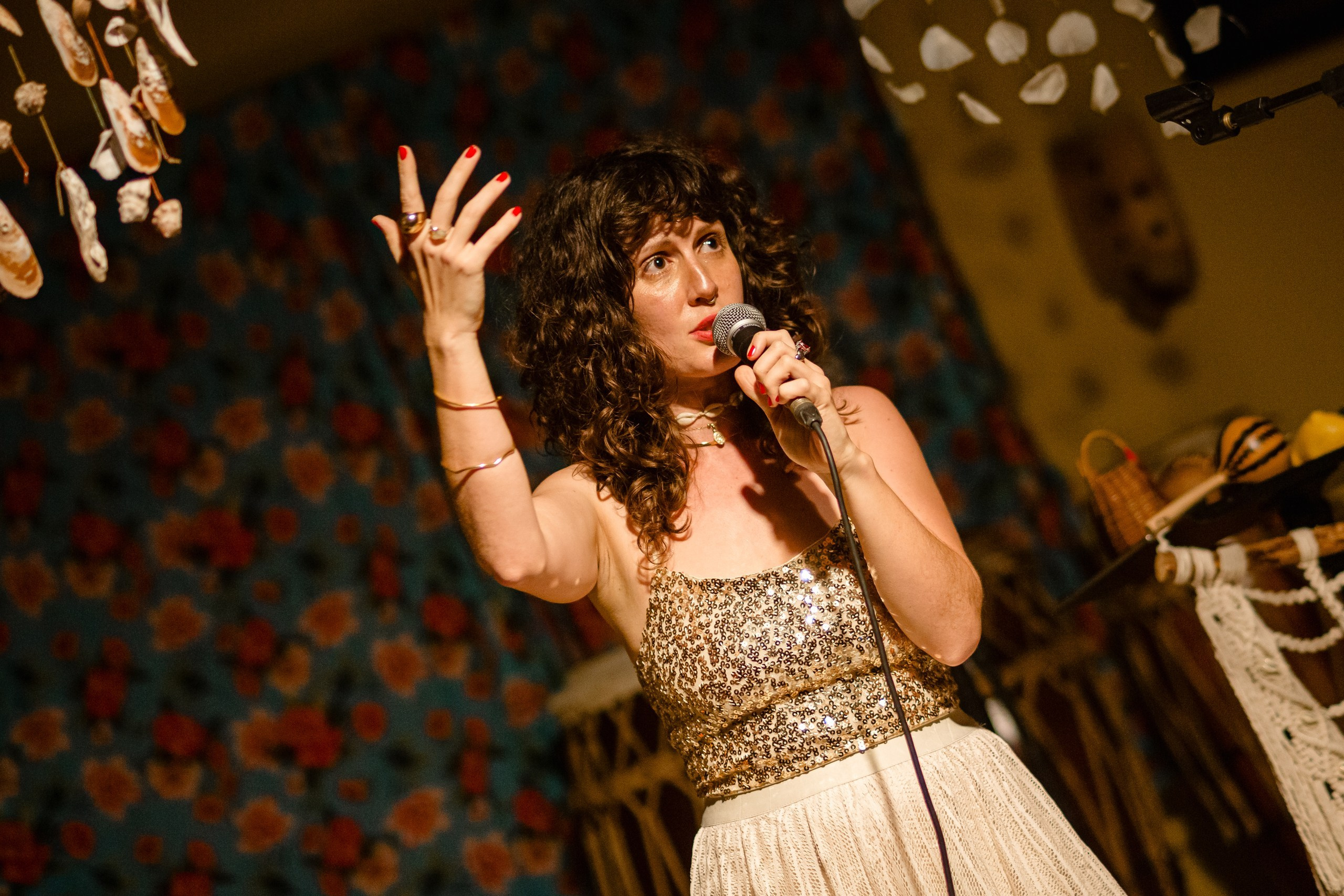 Fotógrafo de show em Balneário Camboriú; a cantora Joana Gaia performando com expressividade e gesto com a mão ao microfone no palco do bairro da Barra para a divulgação do álbum "Água Brasileira".