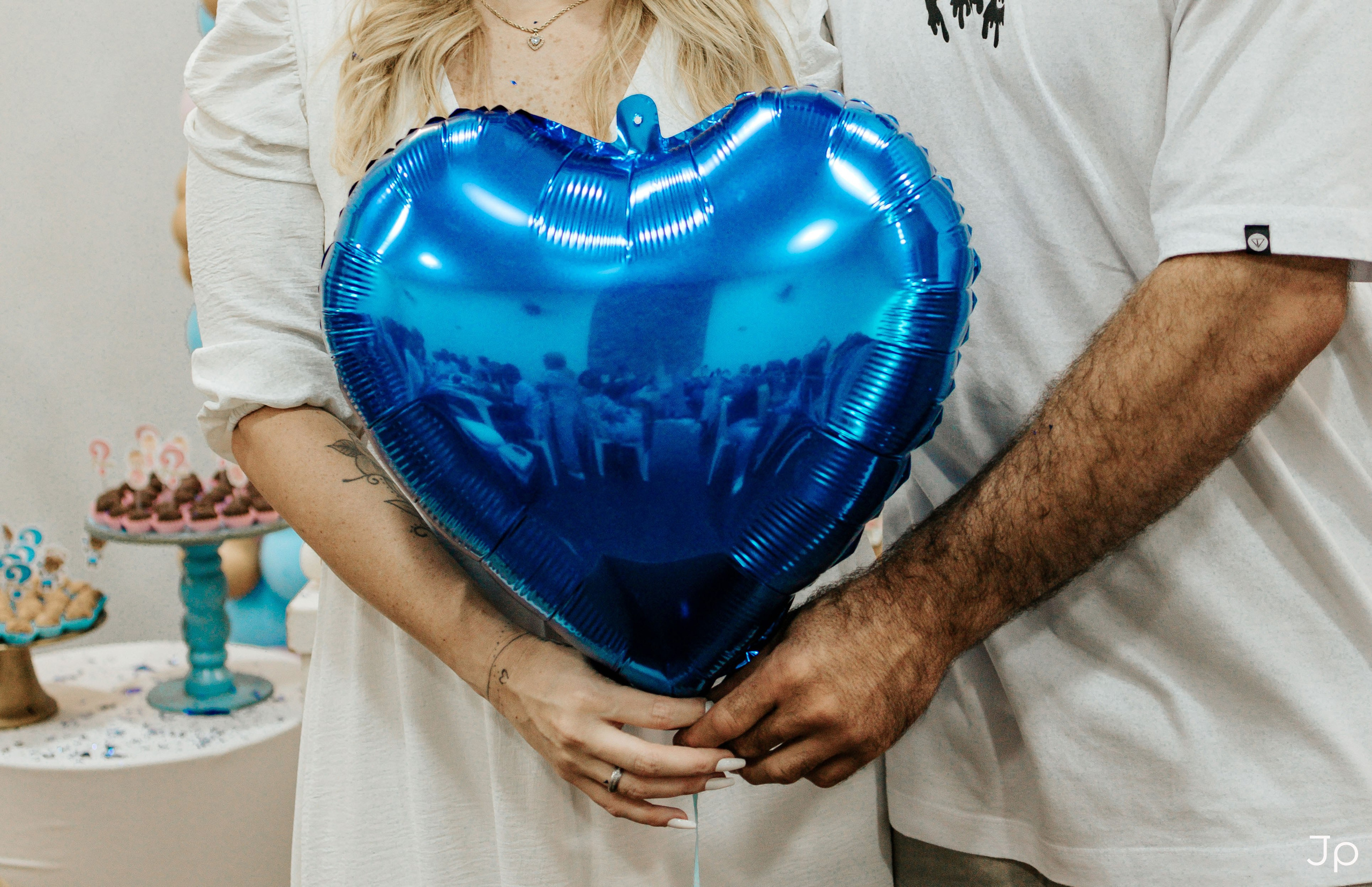 Mão segurando bexiga azul metálica em formato de coração.
