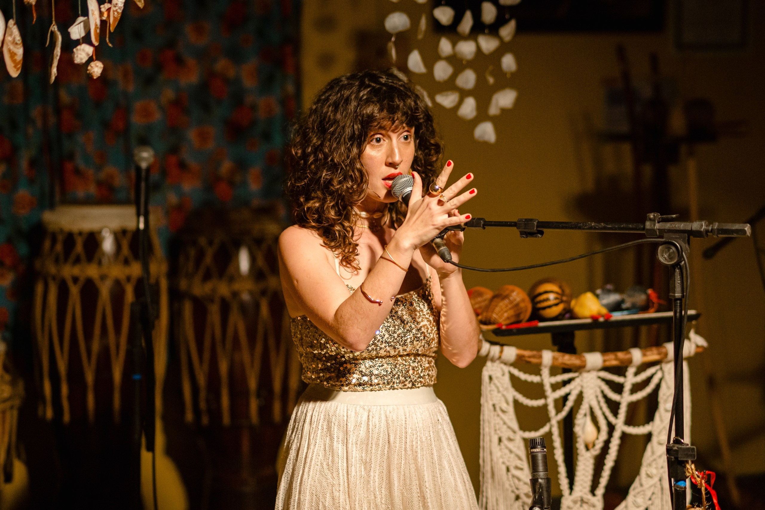 Cobertura fotográfica de show em Balneário Camboriú; a cantora Joana Gaia performando ao vivo no bairro da Barra com microfone e figurino brilhante para divulgação do álbum "Água Brasileira".