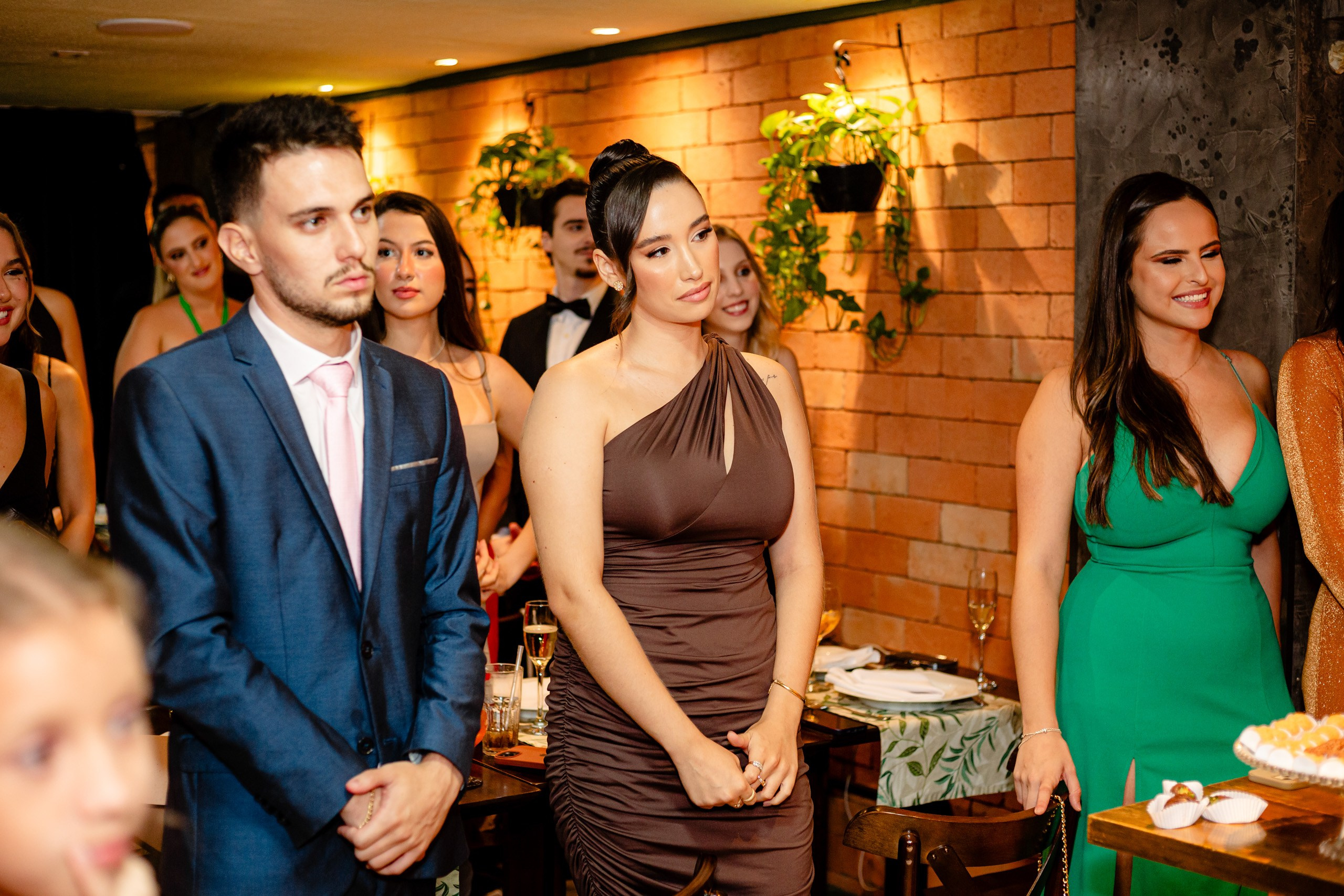 Fotógrafo de formatura em Balneário Camboriú; convidados atentos e sorridentes acompanham o momento da festa em ambiente com parede de tijolos aparentes.