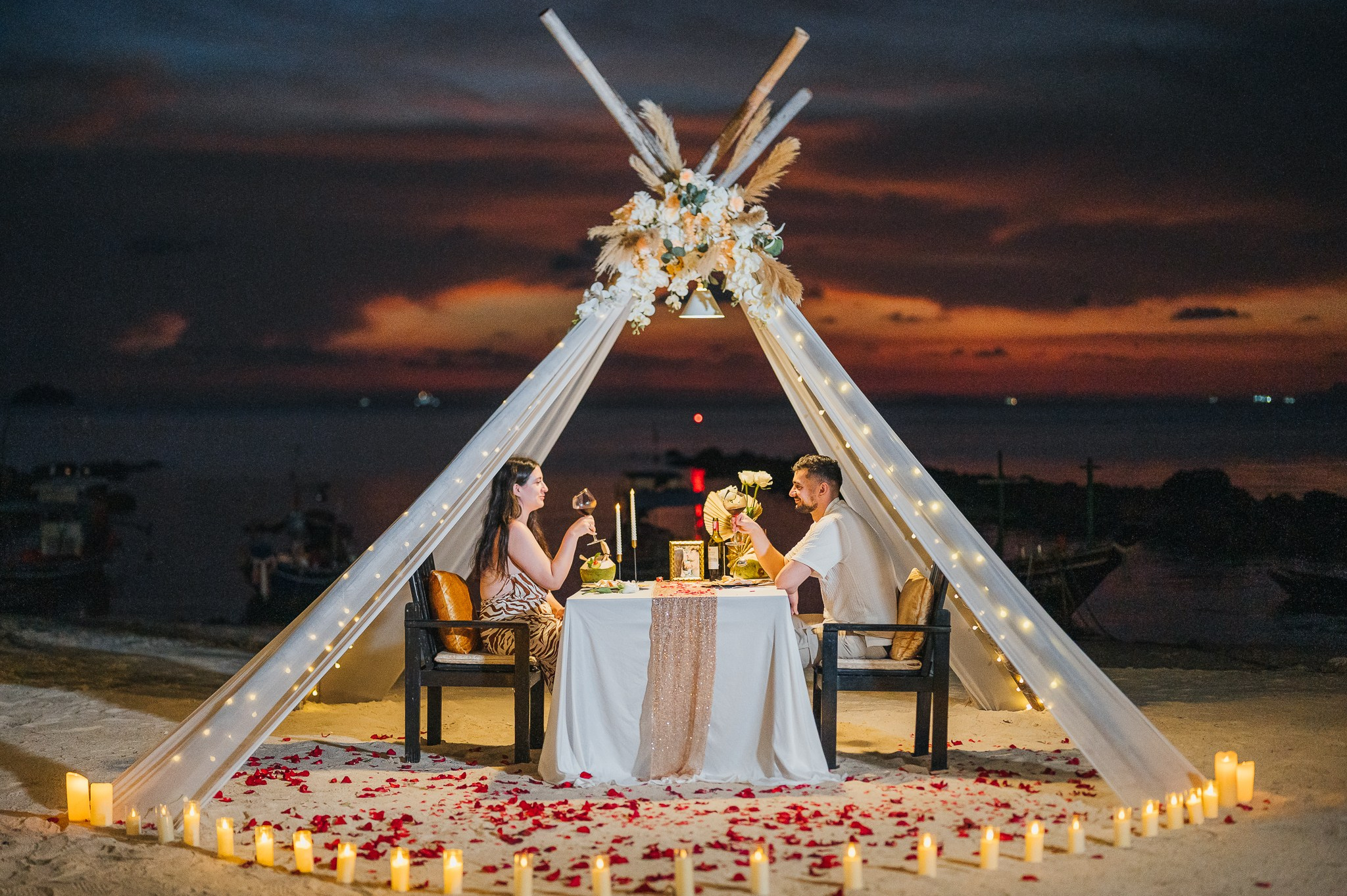 Romantic beach proposal setup in Koh Samui, Thailand with candles, flowers and ocean sunset view.