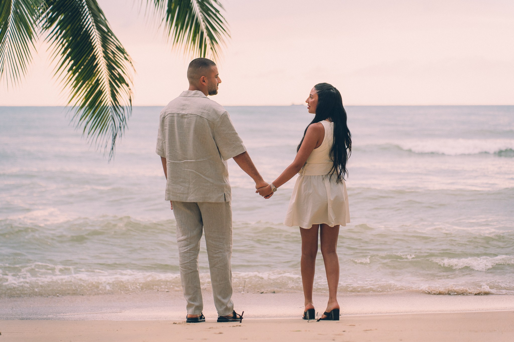 Romantic couple holding hands on a Pattaya beach at sunset after their marriage proposal.