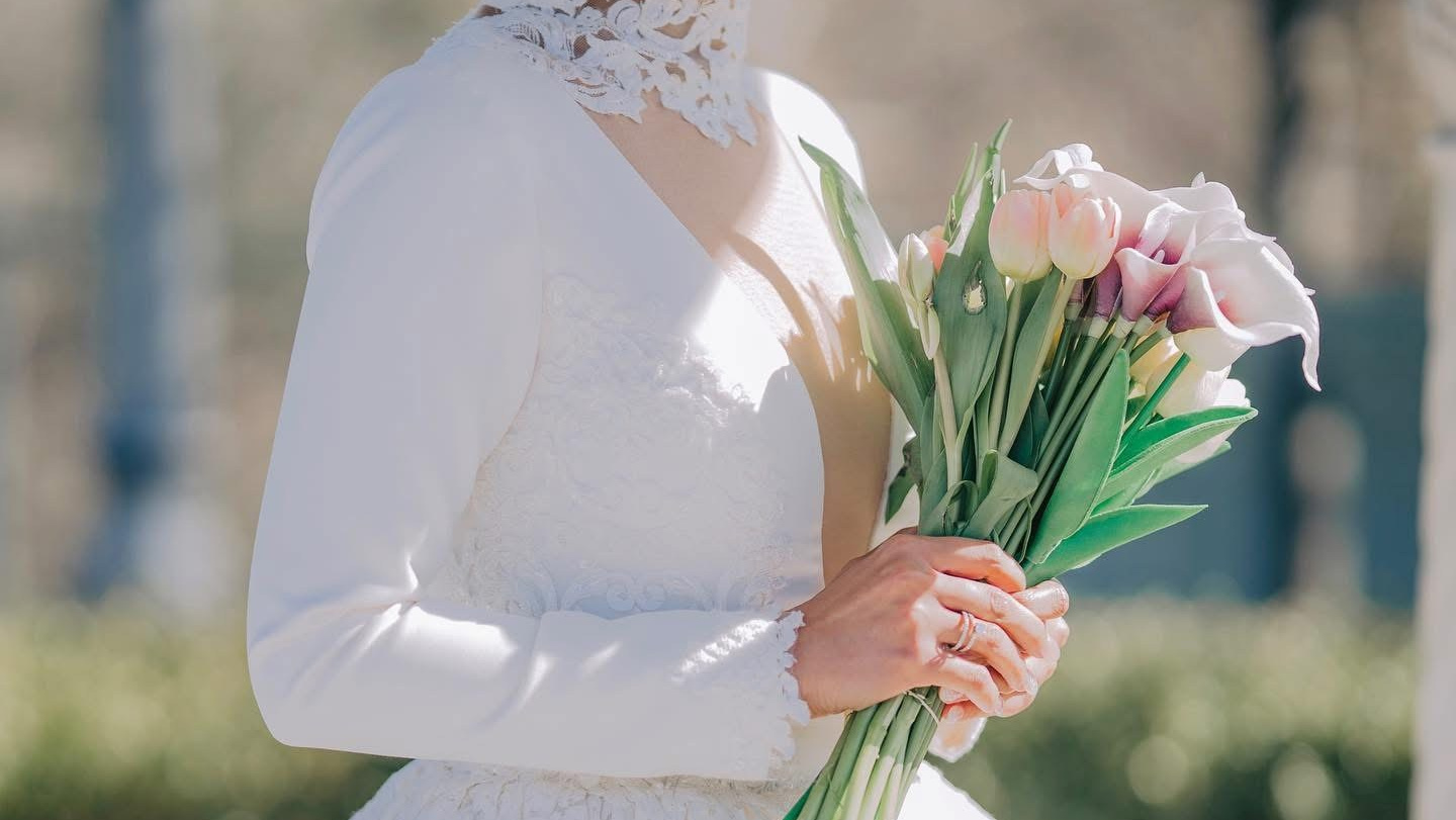 Bride in white wedding gown holding a floral bouquet outdoors