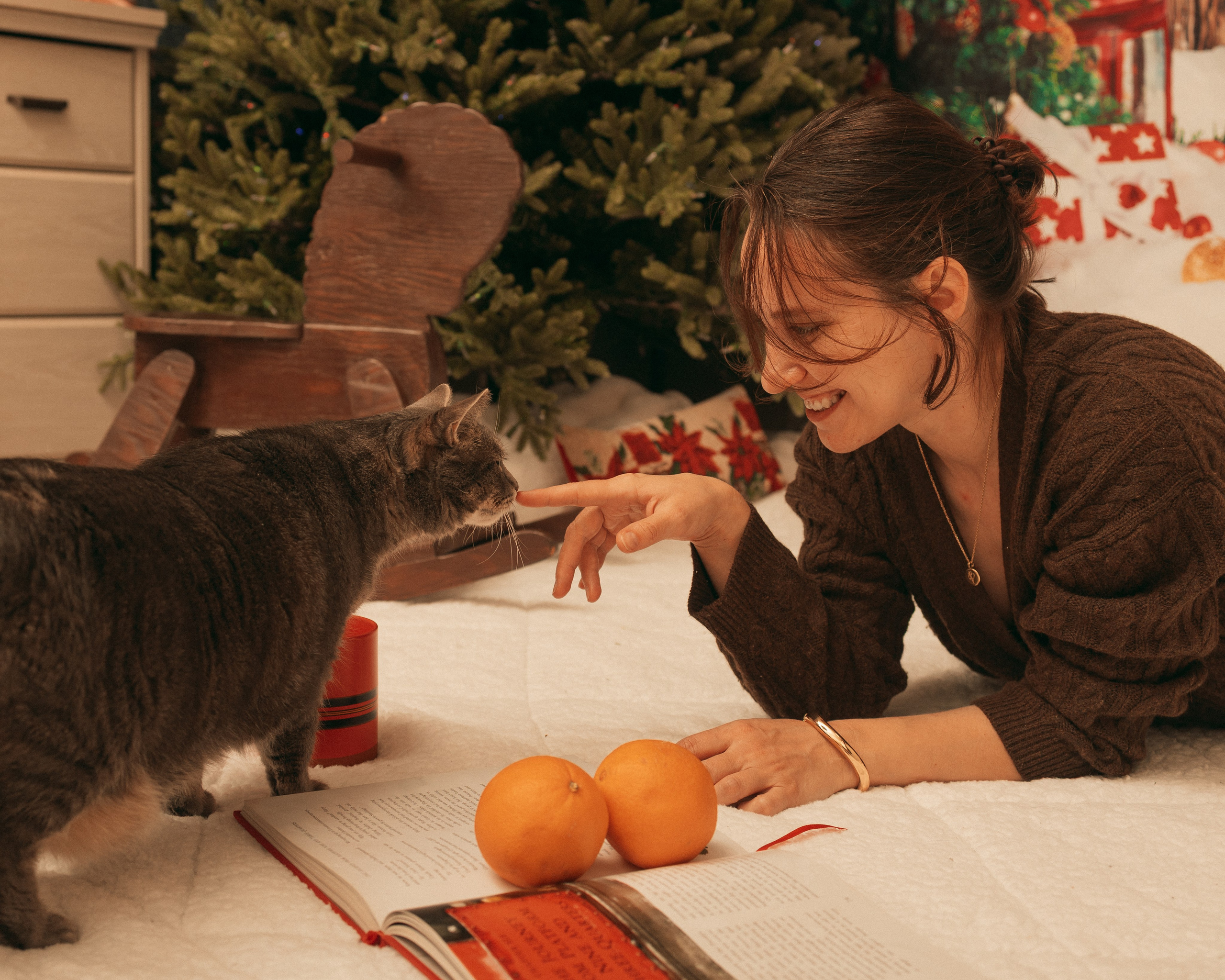 Woman sharing a playful moment with her grey cat beside a decorated Christmas tree.