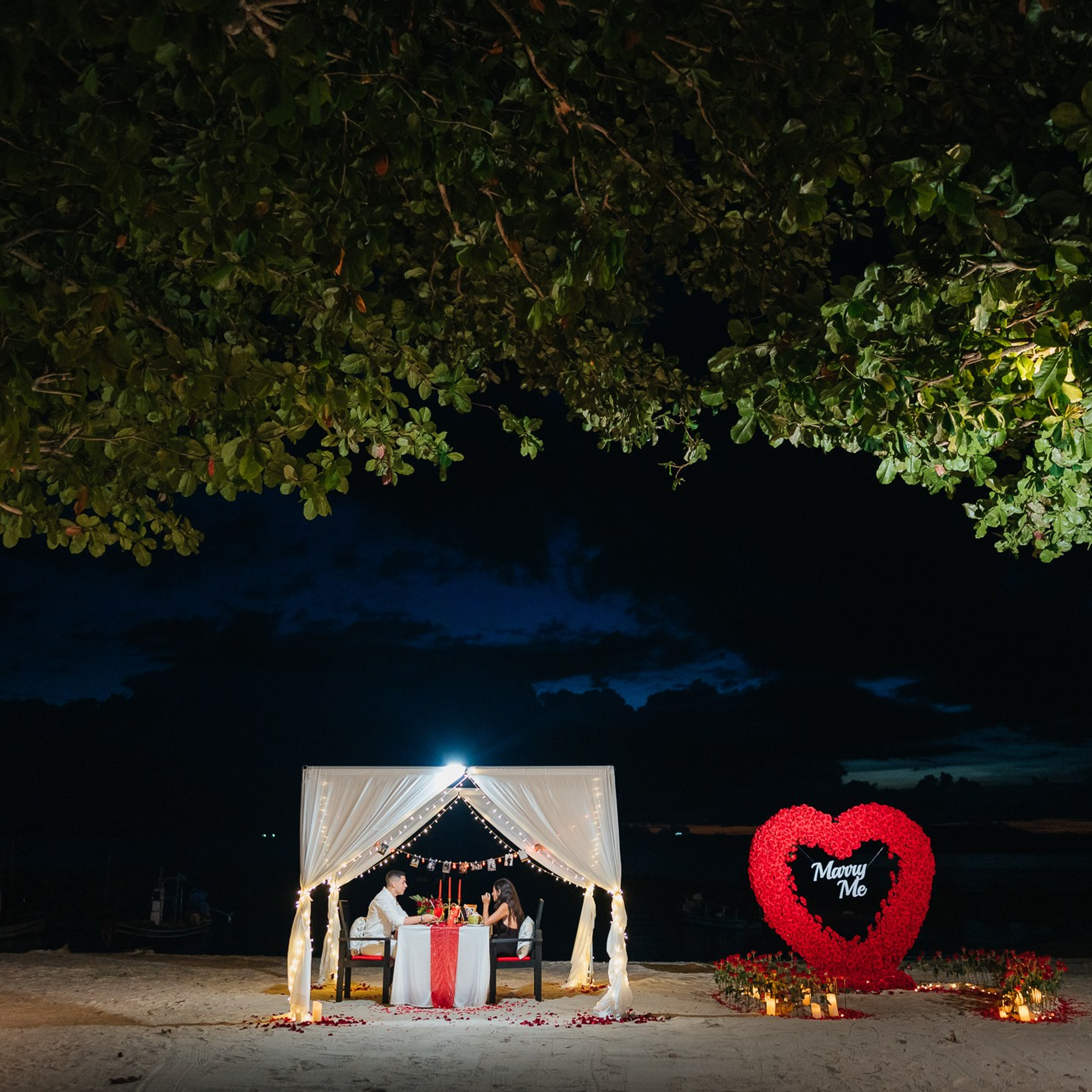 Romantic beach proposal setup in Koh Samui with candles and flower arch.