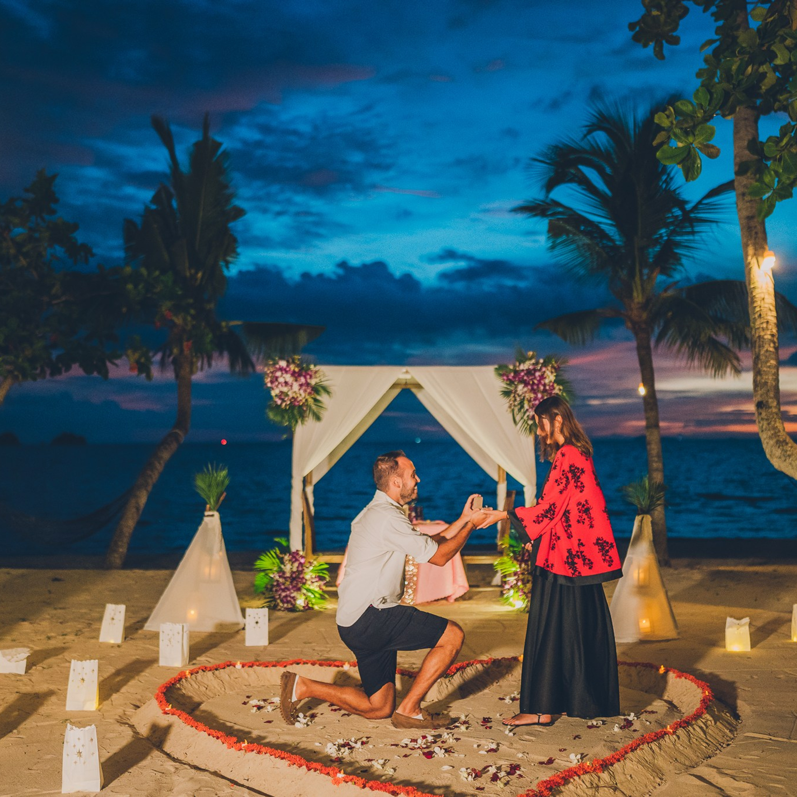 Romantic beach proposal setup in Koh Samui with candles and flower arch.