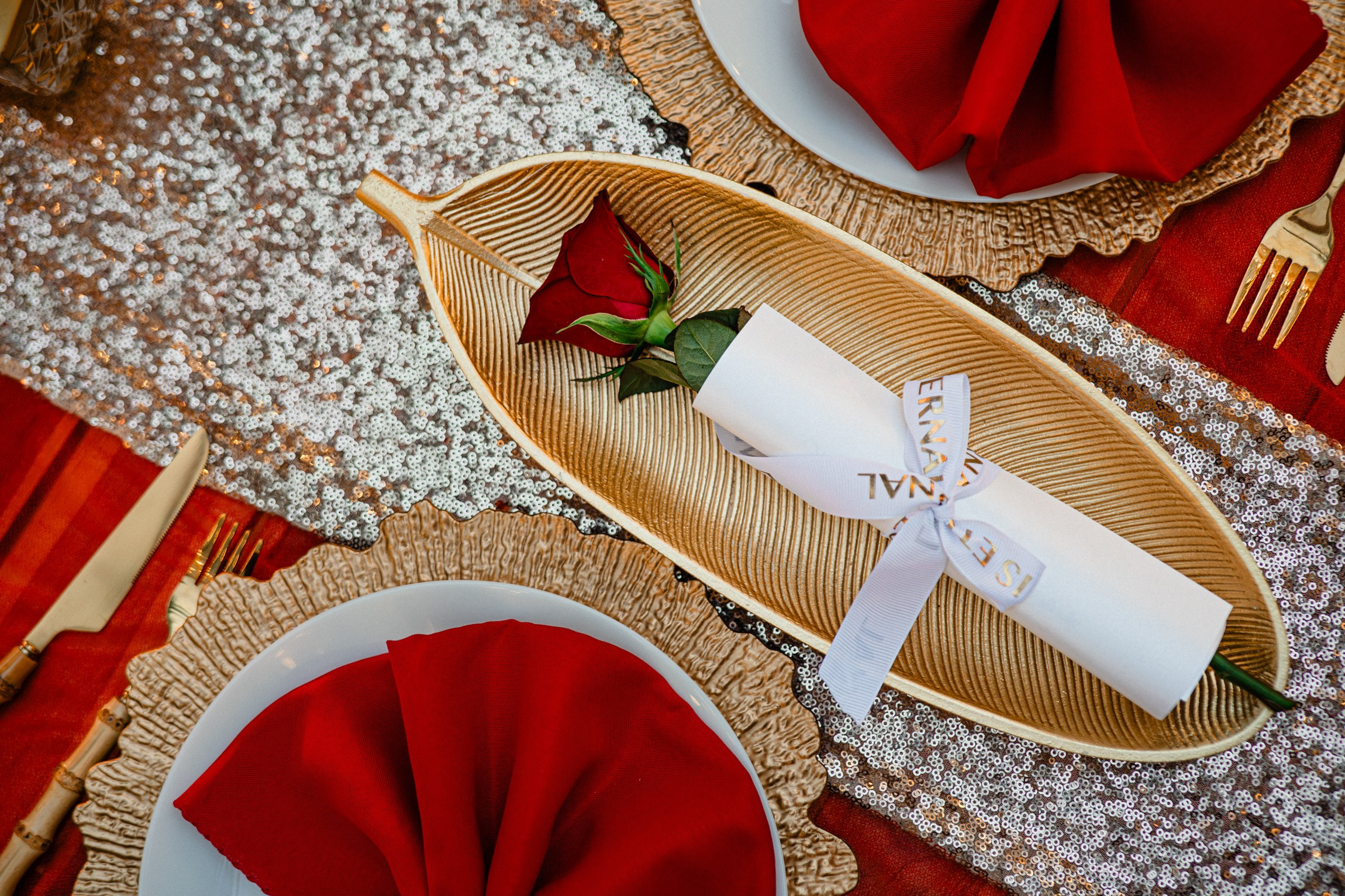 Romantic dinner table setting in Koh Samui with a red rose, elegant gold décor and personalized details.