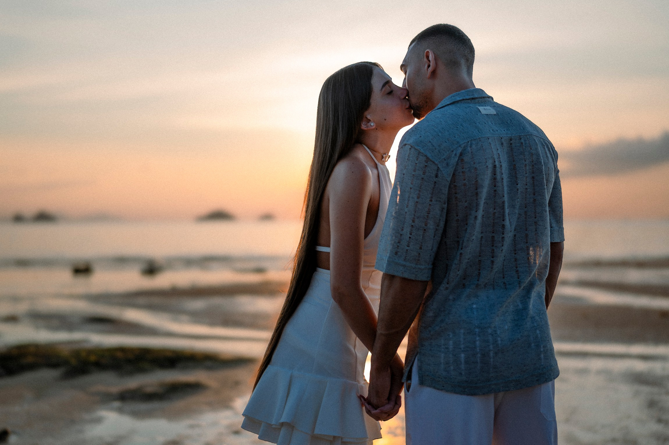 Romantic couple holding hands on a Pattaya beach at sunset after their marriage proposal.