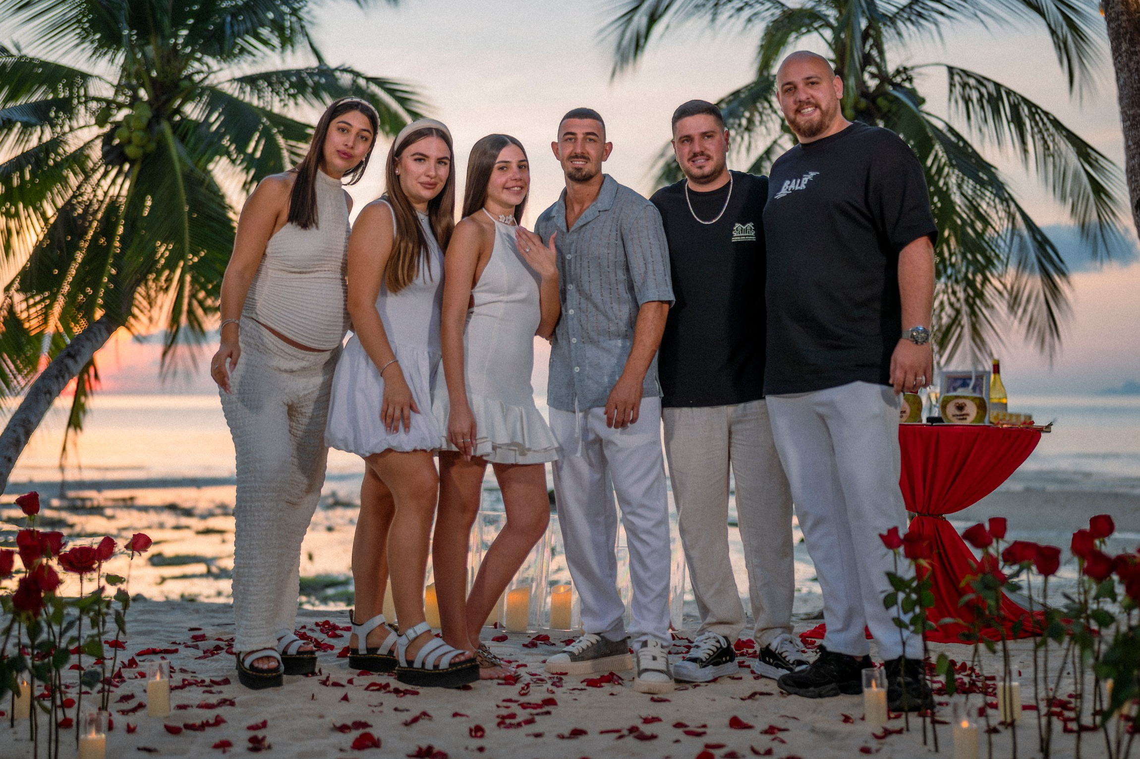 Newly engaged couple celebrating their beach proposal in Pattaya with friends beside romantic decorations.