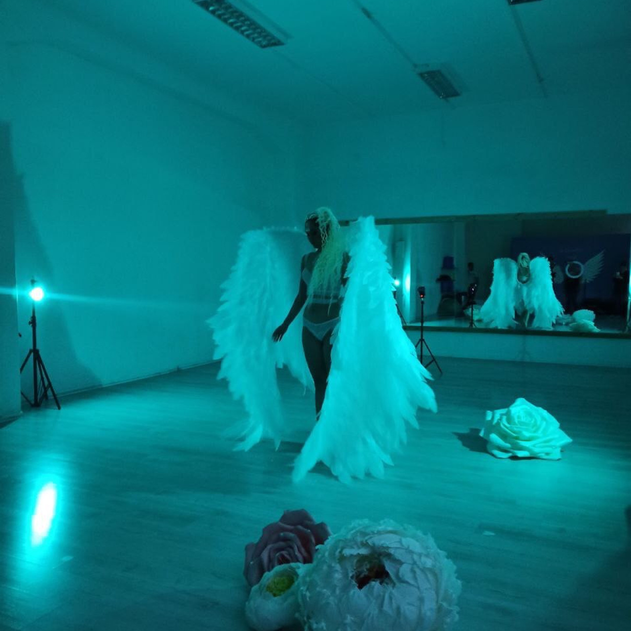 Behind the scenes creative studio photography session with dramatic teal lighting and angel wings prop