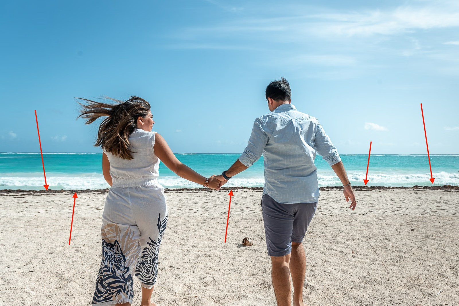 Couple running hand in hand during a love story photoshoot on Bavaro Beach with Sargassum