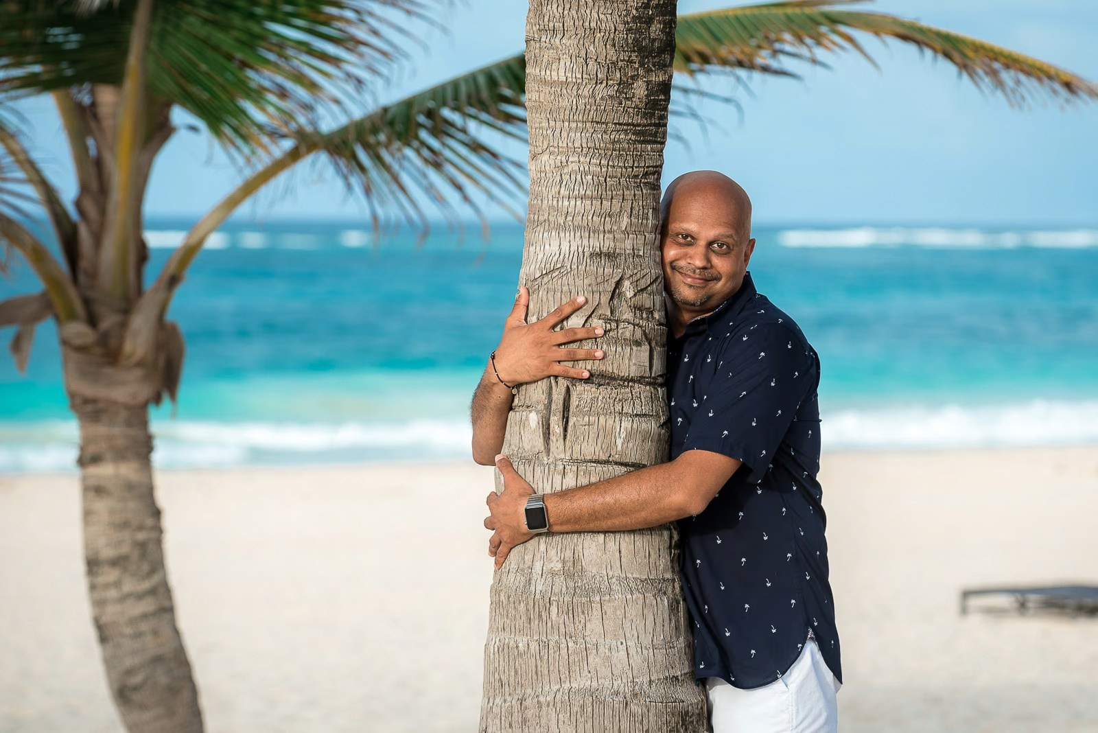 Hombre abrazando una palmera durante una sesión de fotos en la playa Bávaro en Punta Cana