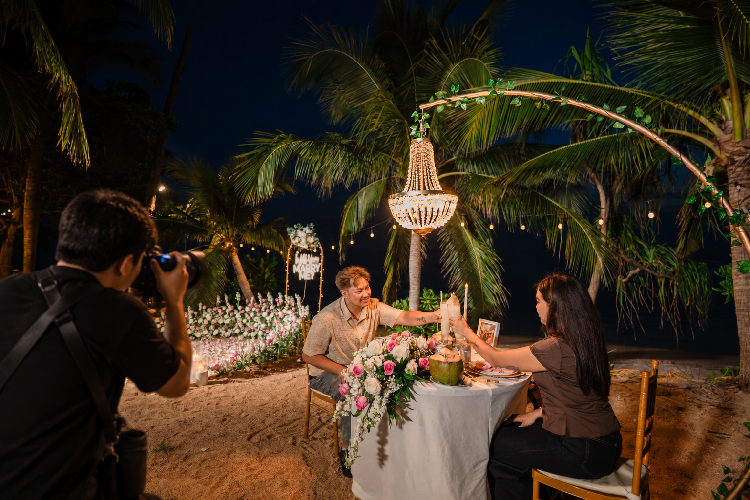 Marriage proposal photographer capturing a couple during a romantic beach dinner in Koh Samui with flowers, candles and tropical palm trees.