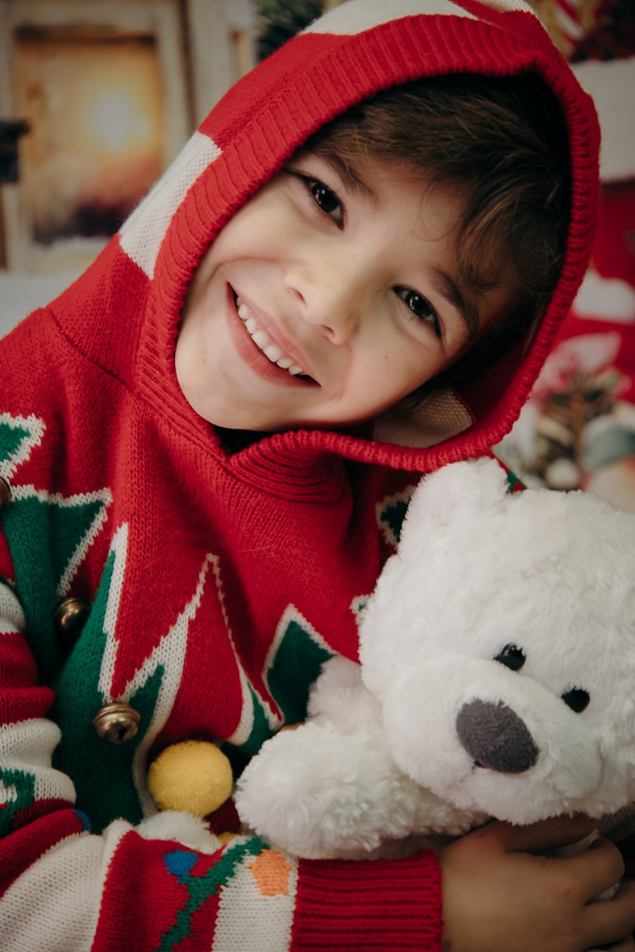 Portrait of a young boy in a festive Christmas sweater holding a teddy bear in a beautifully decorated Christmas photography studio in Calgary.