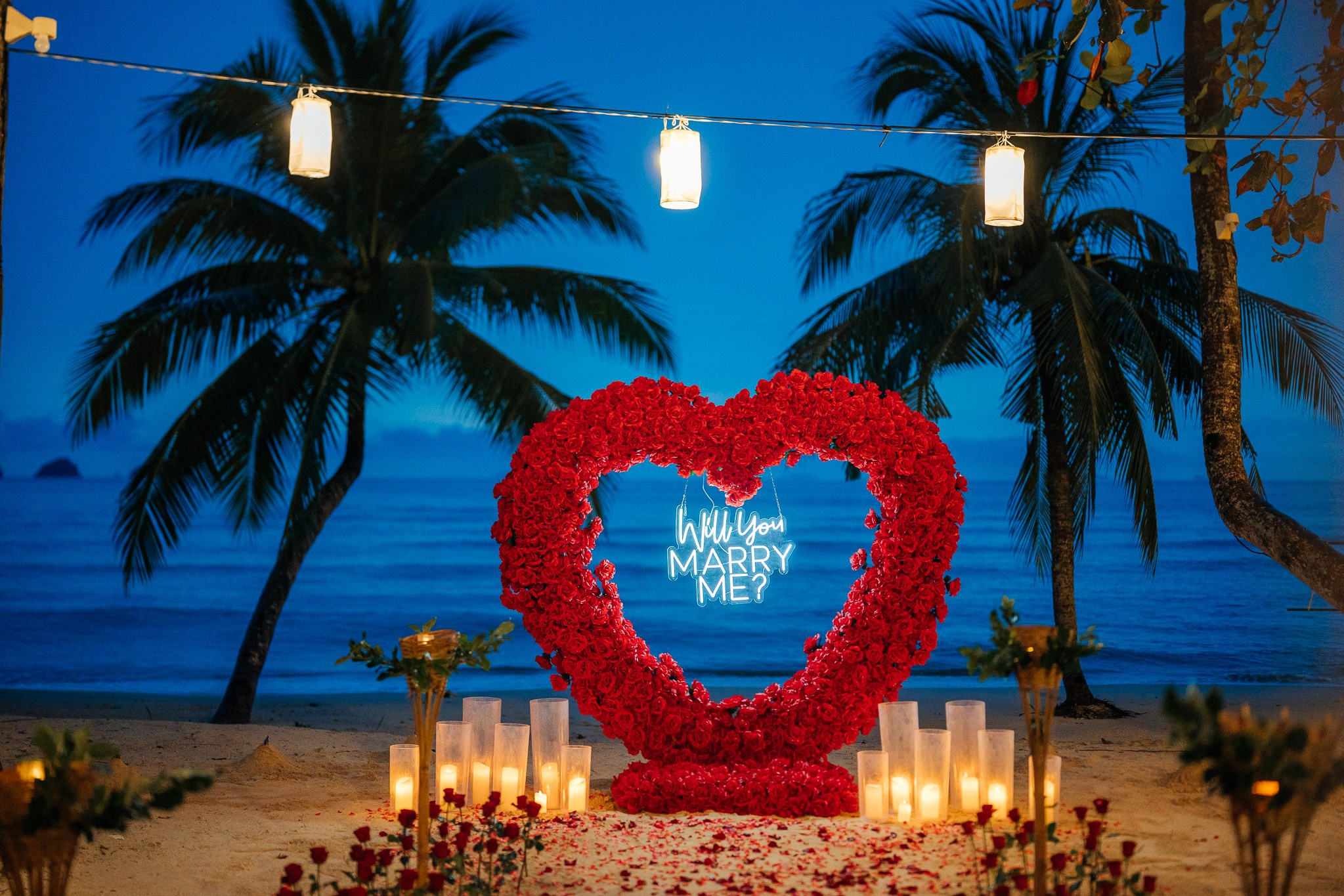 Romantic beach proposal setup in Koh Samui, Thailand with candles, flowers and ocean sunset view.