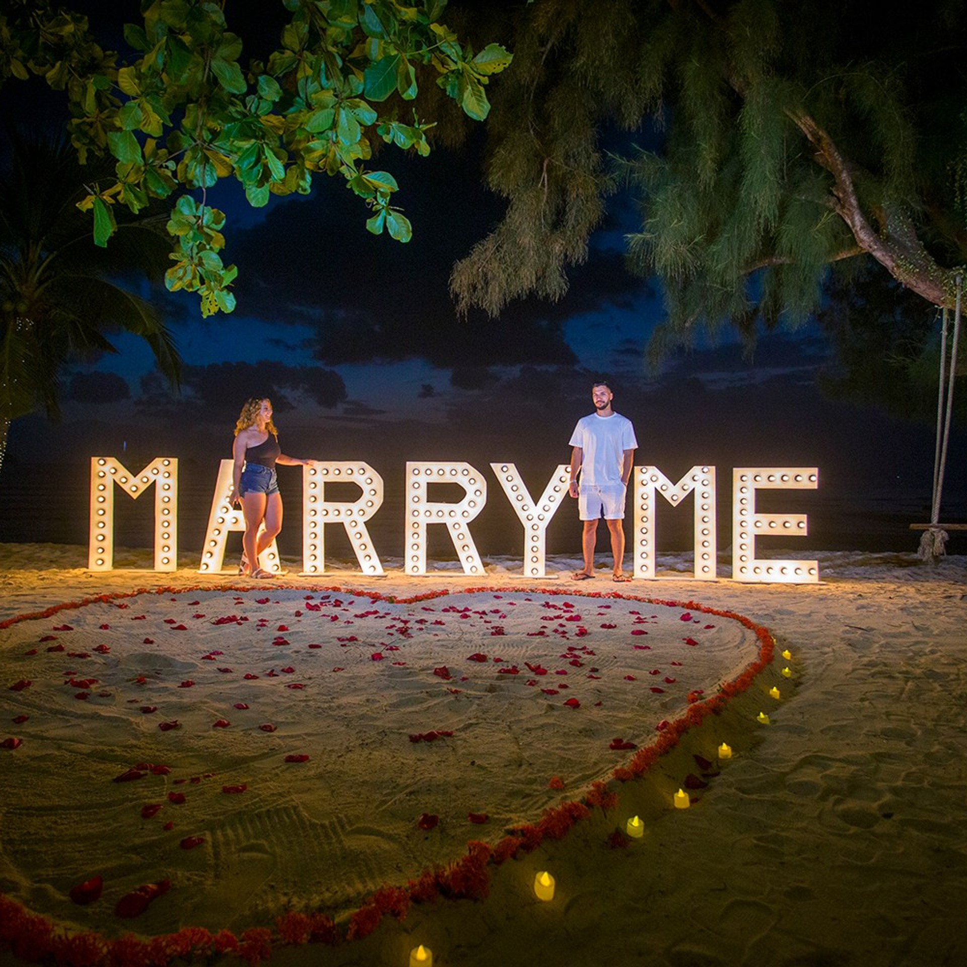 Romantic beach proposal setup in Koh Samui with candles and flower arch.