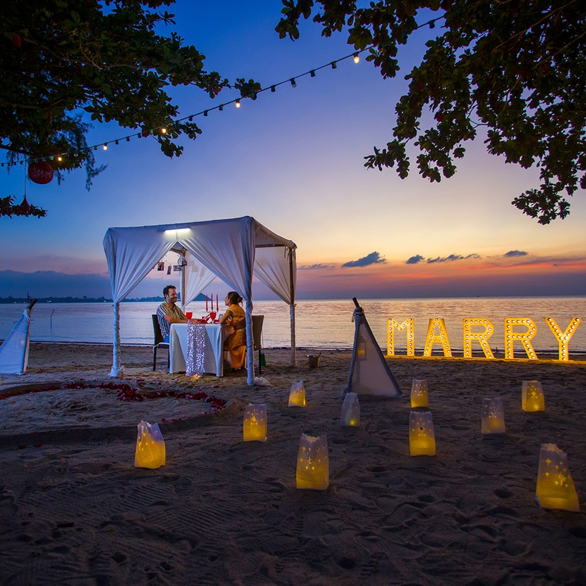 Romantic beach proposal setup in Koh Samui with candles and flower arch.