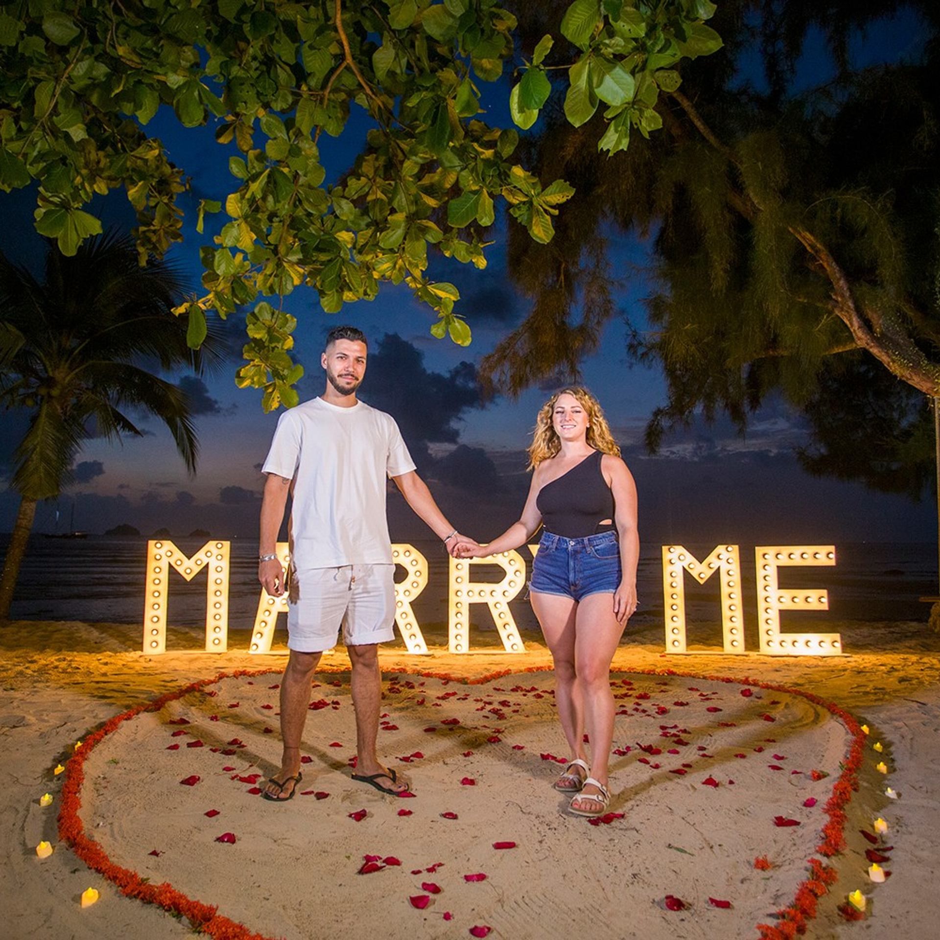 Romantic beach proposal setup in Koh Samui with candles and flower arch.