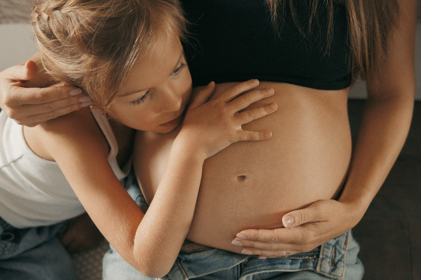 Older child leaning close to their mother’s pregnant belly at home in Montreal