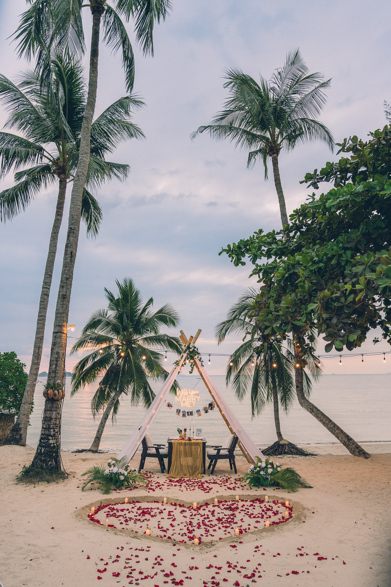 Romantic beach proposal setup in Pattaya with palm trees, rose petals and an intimate seaside table.