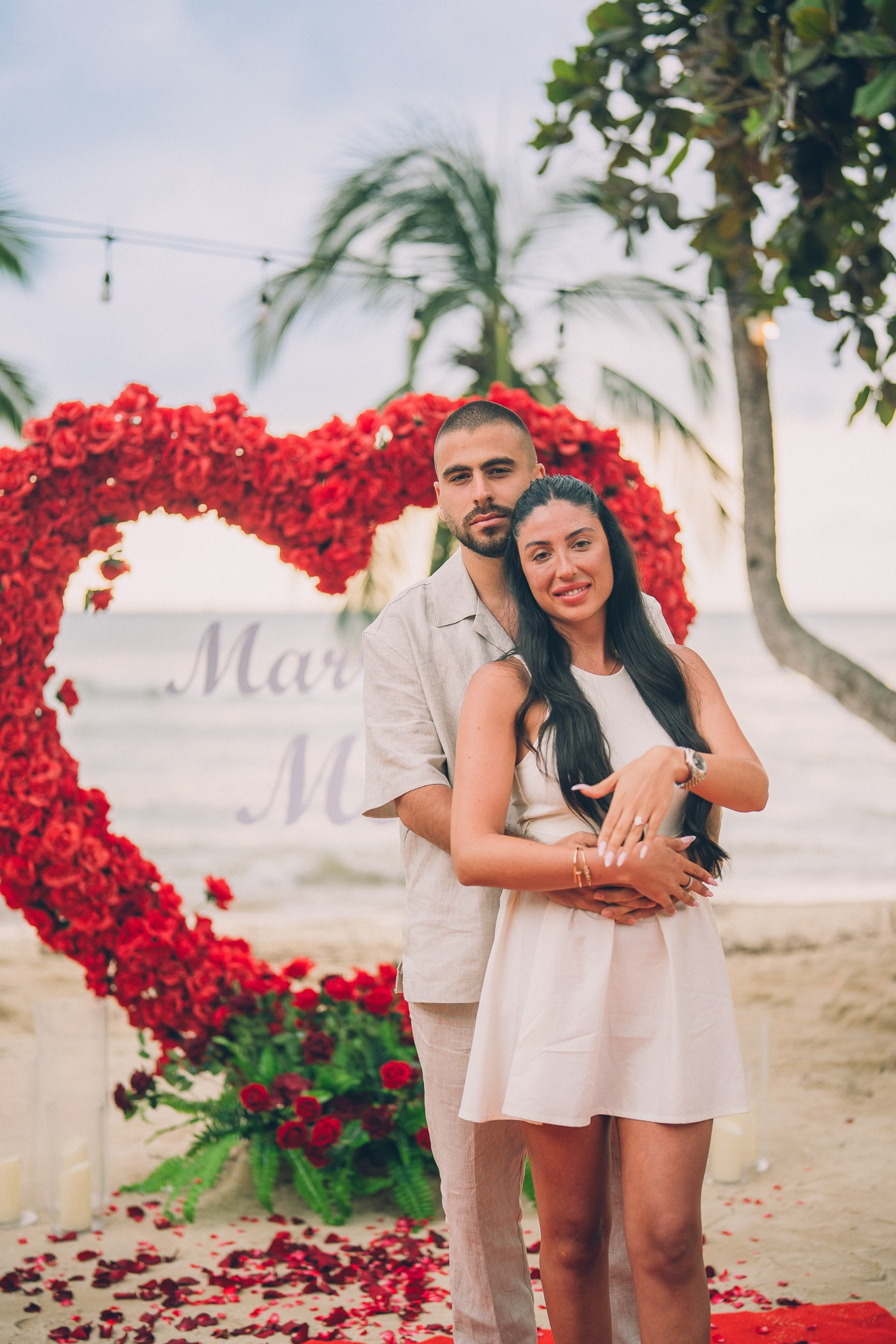 Newly engaged couple posing in front of a red rose heart arch after a romantic beach proposal in Pattaya.