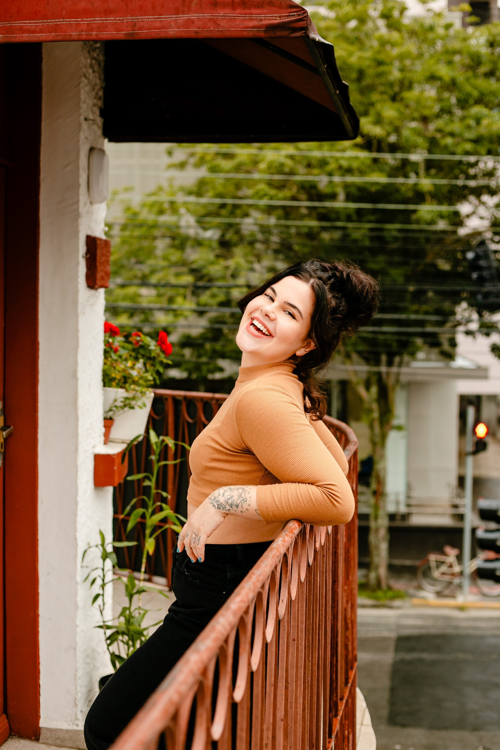 Mulher sorrindo encostada em grade com fundo de árvore.