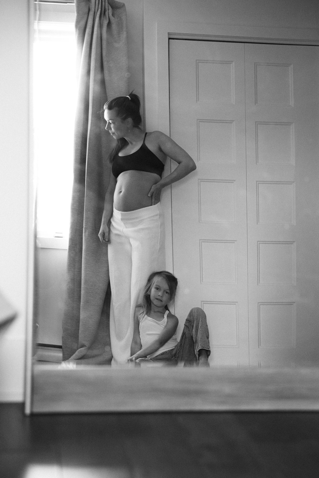 Expectant mother standing by a window with her daughter at home in Montreal